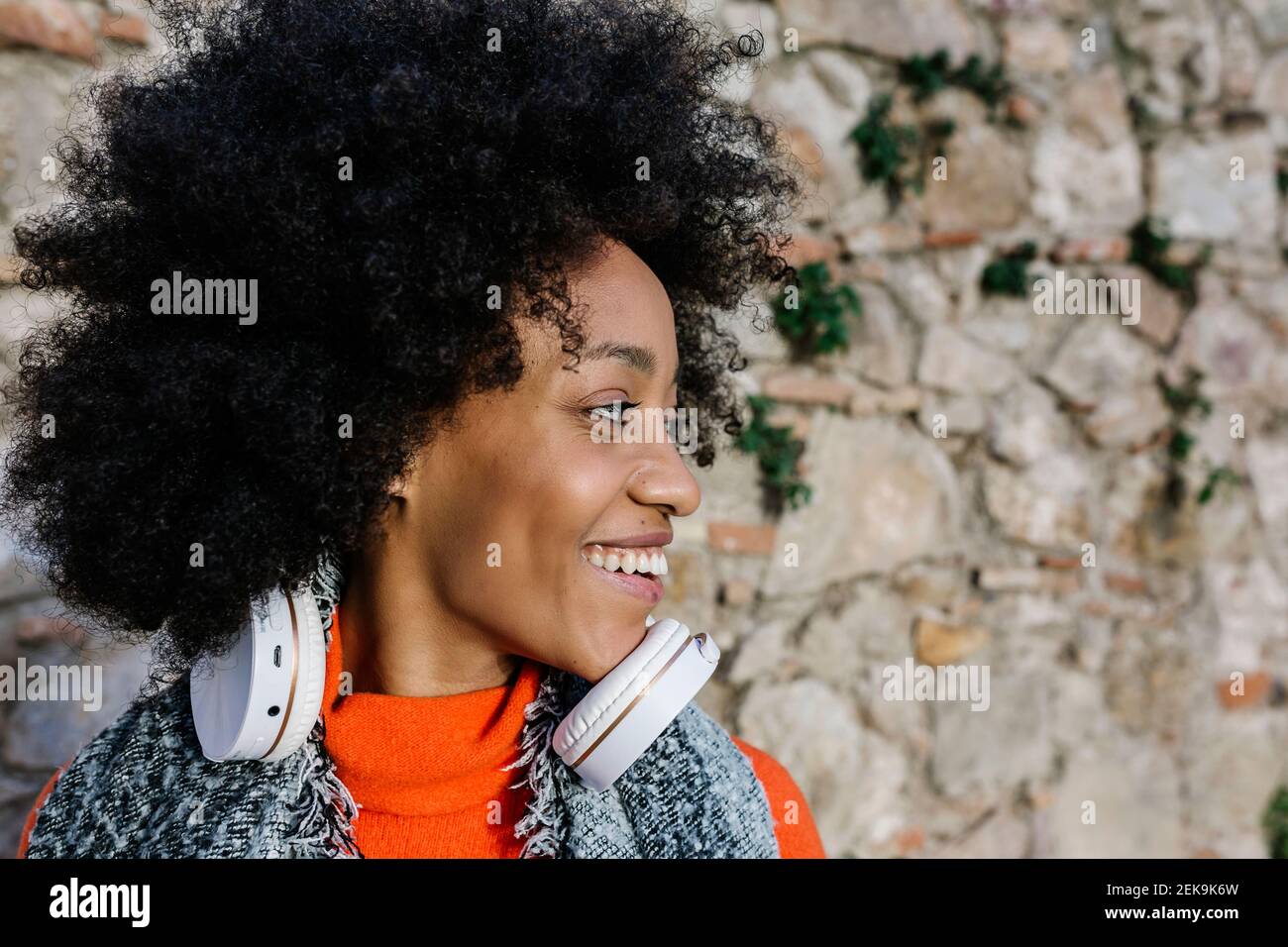 Fröhliche Afro-Frau mit Kopfhörern, die gegen die Steinwand schaut Stockfoto