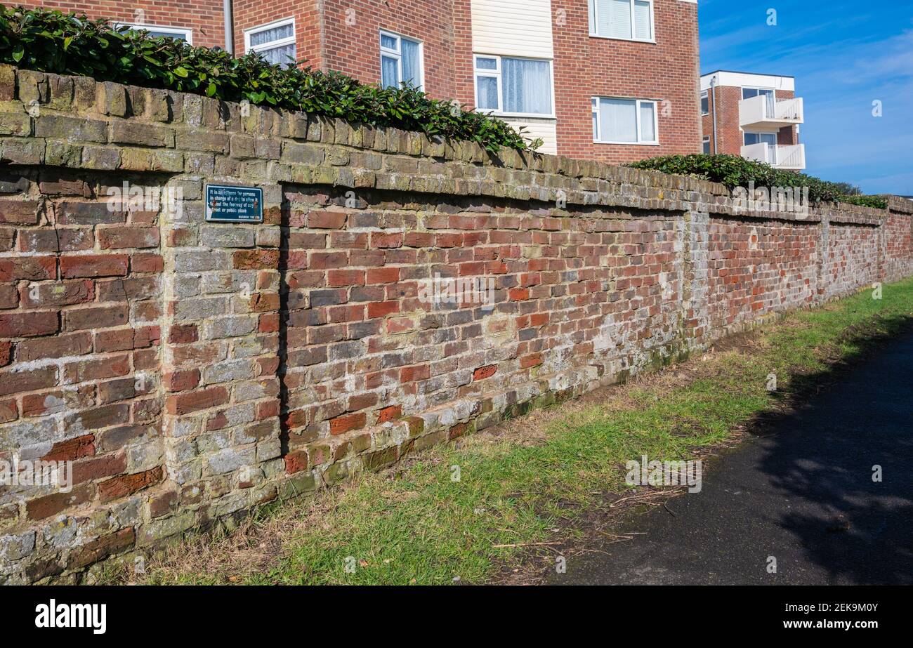 Eine alte, verblasste, verwitterte und abgenutzte rote Ziegelmauer entlang einer Gasse in West Sussex, England, Großbritannien. Stockfoto