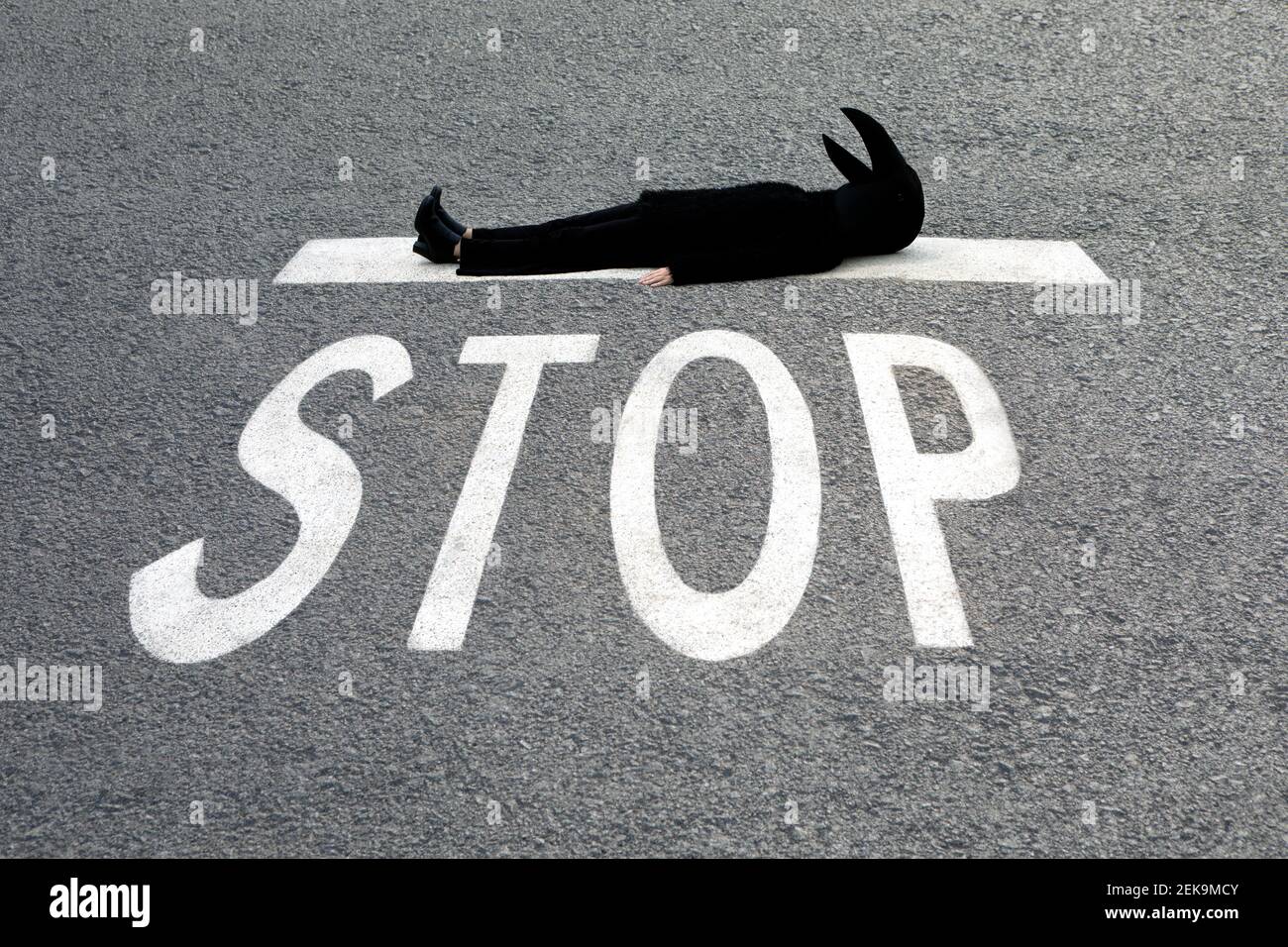 Frau im Krähenkostüm, die am STOPPSCHILD liegt Straße Stockfoto