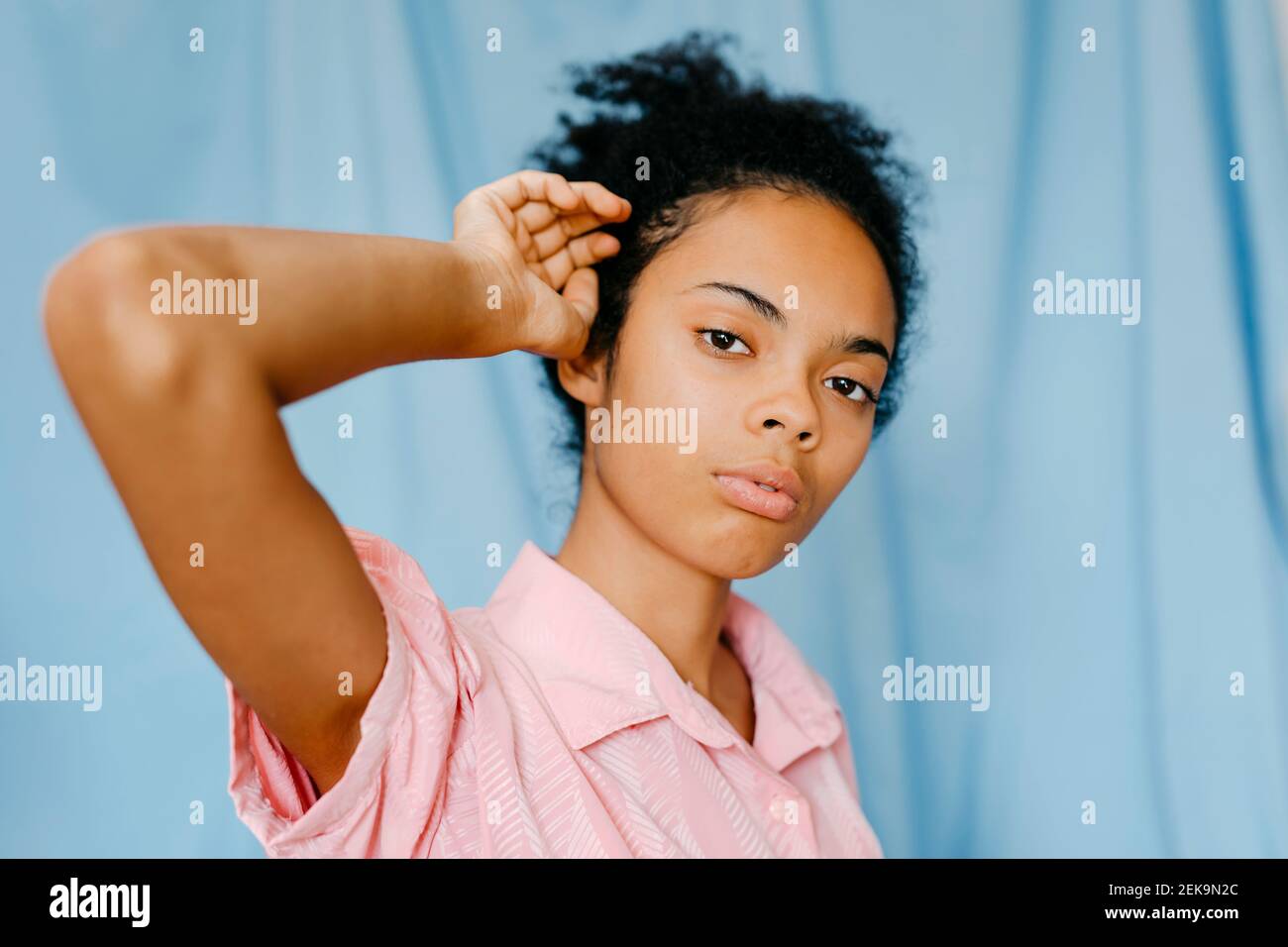 Betrachtende Frau mit der Hand im Haar gegen den blauen Vorhang Stockfoto