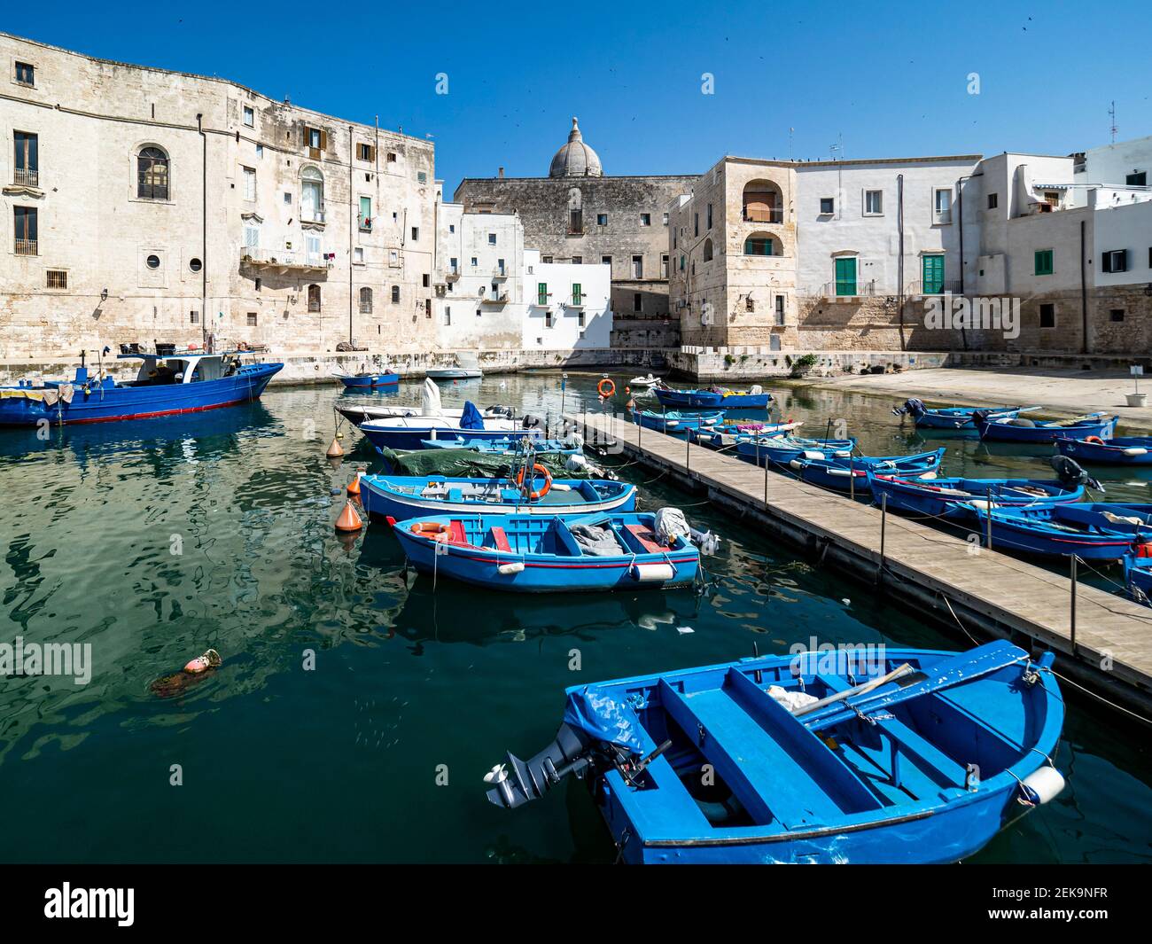 Blaues Boot, das an sonnigen Tagen in Monopoli, Apulien, Italien, in einem Kanal von Gebäuden vertäut ist Stockfoto