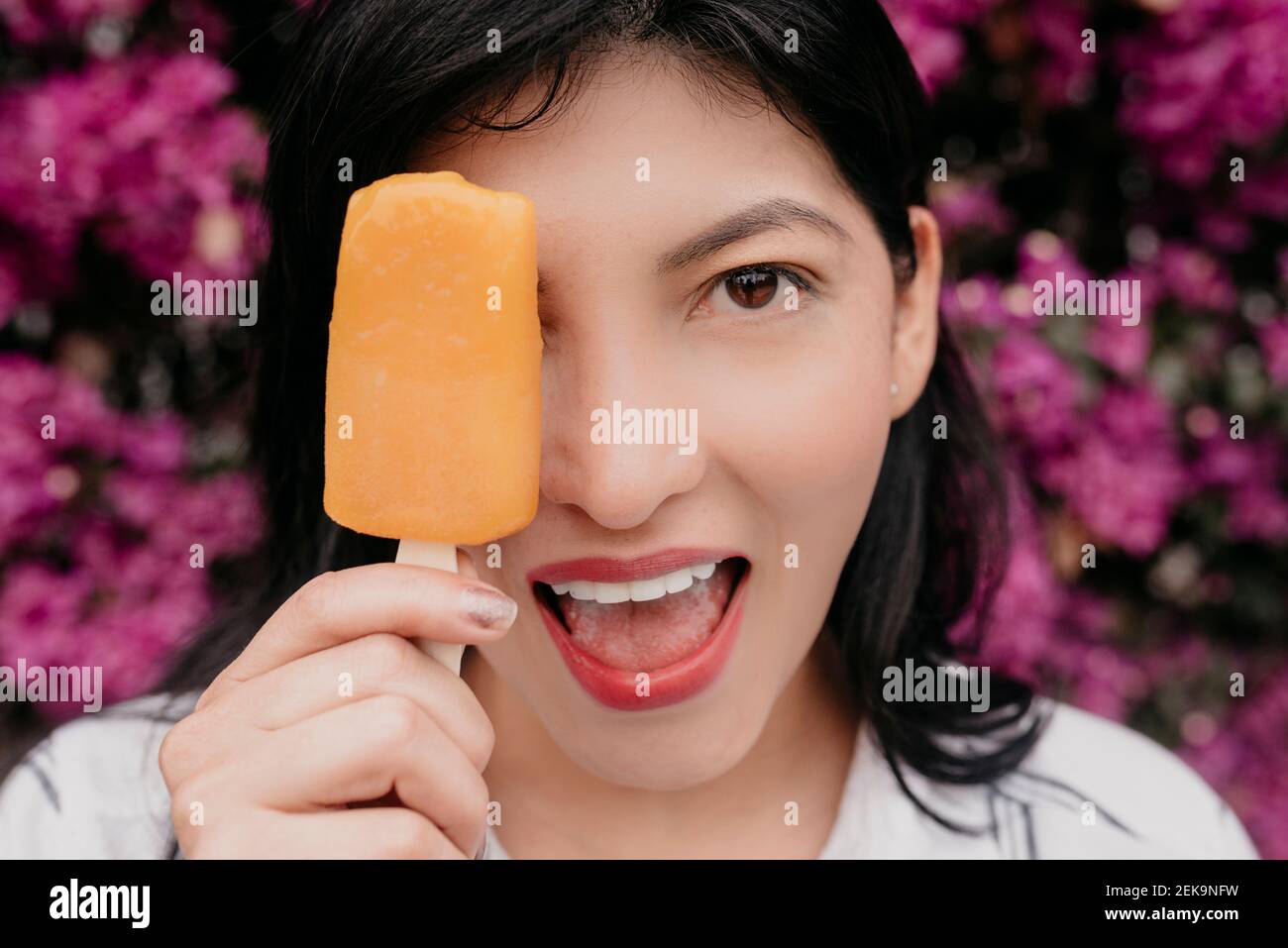 Glückliche Frau mit offenem Mund, das Auge mit orangefarbenem Eis bedeckt Creme Stockfoto