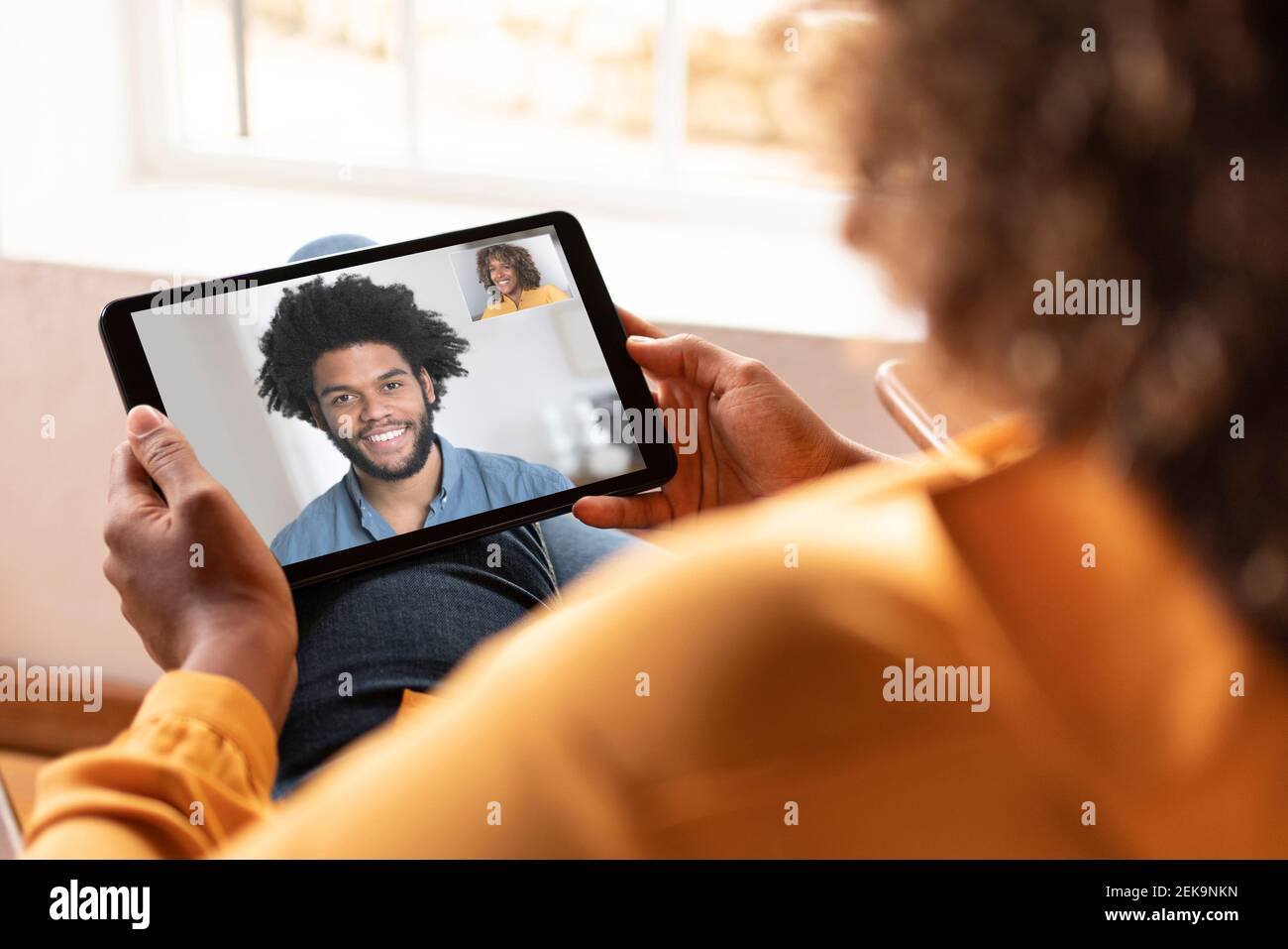 Frau im Gespräch mit lächelndem Mann auf Videoanruf durch digital Tablet, während Sie zu Hause sitzen Stockfoto