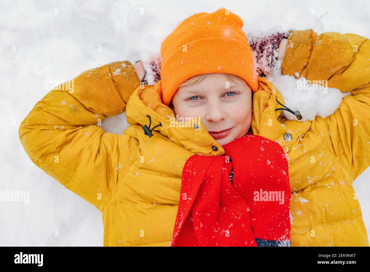 Junge in warmer Kleidung mit Händen hinter dem Kopf liegend Schnee Stockfoto