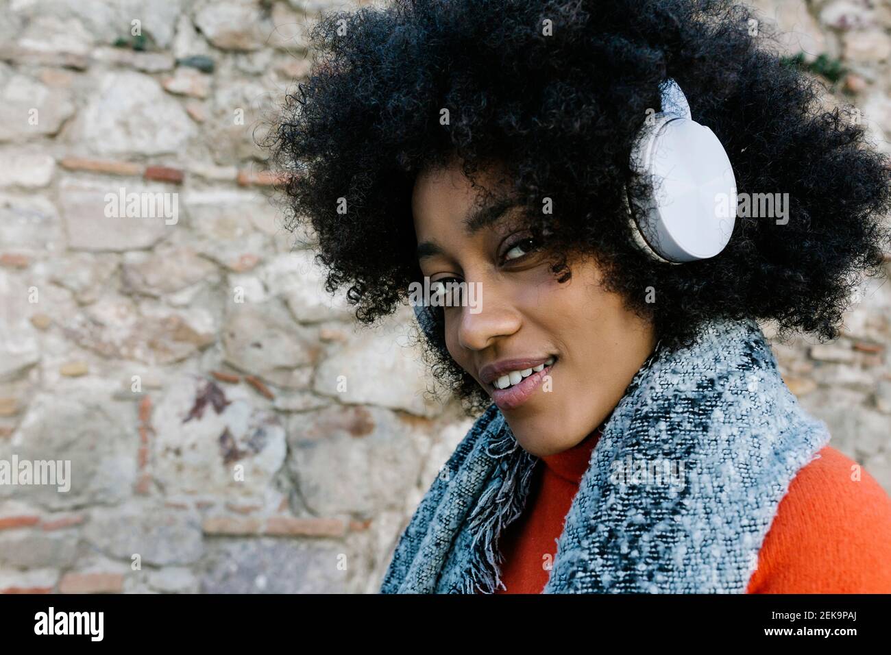 Afro junge Frau, die Musik durch Kopfhörer gegen Steinwand hört Stockfoto