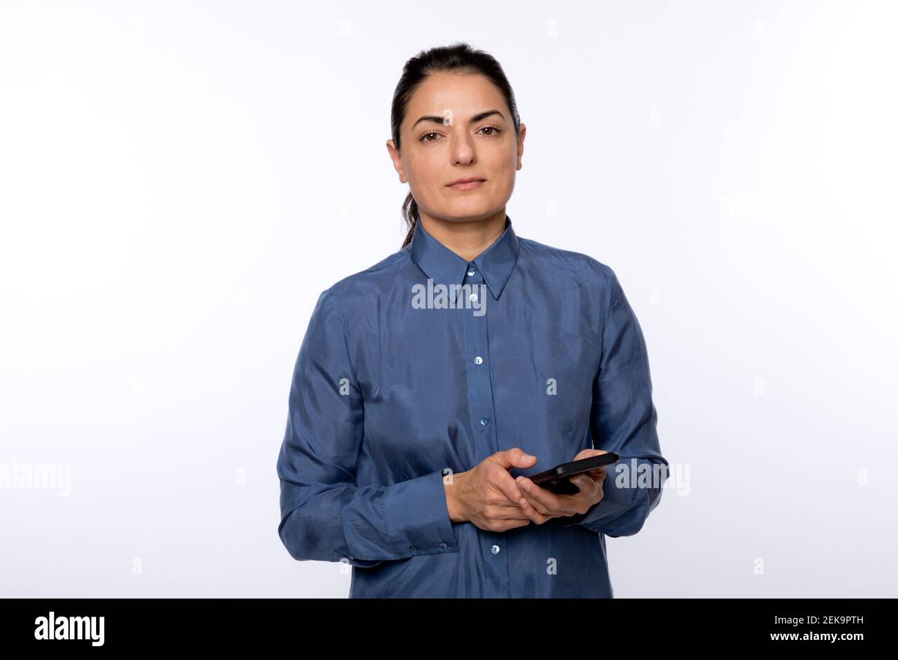 Frau in blauem Hemd mit Smartphone gegen Weiß stehend Hintergrund Stockfoto