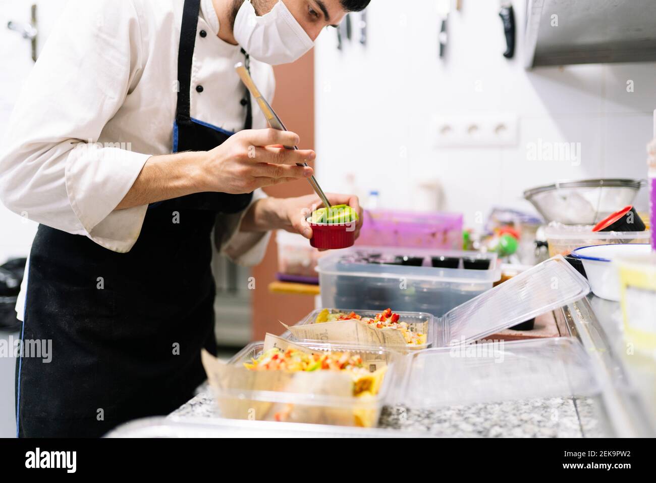 Junger männlicher Koch garniert Essen in der Restaurantküche Während einer Pandemie Stockfoto