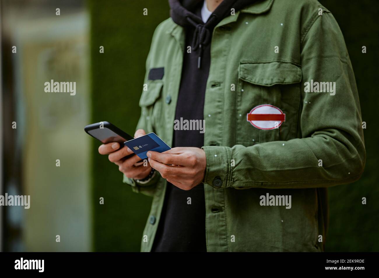 Mann in der Jacke hält Handy beim Online-Shopping Per Kreditkarte Stockfoto