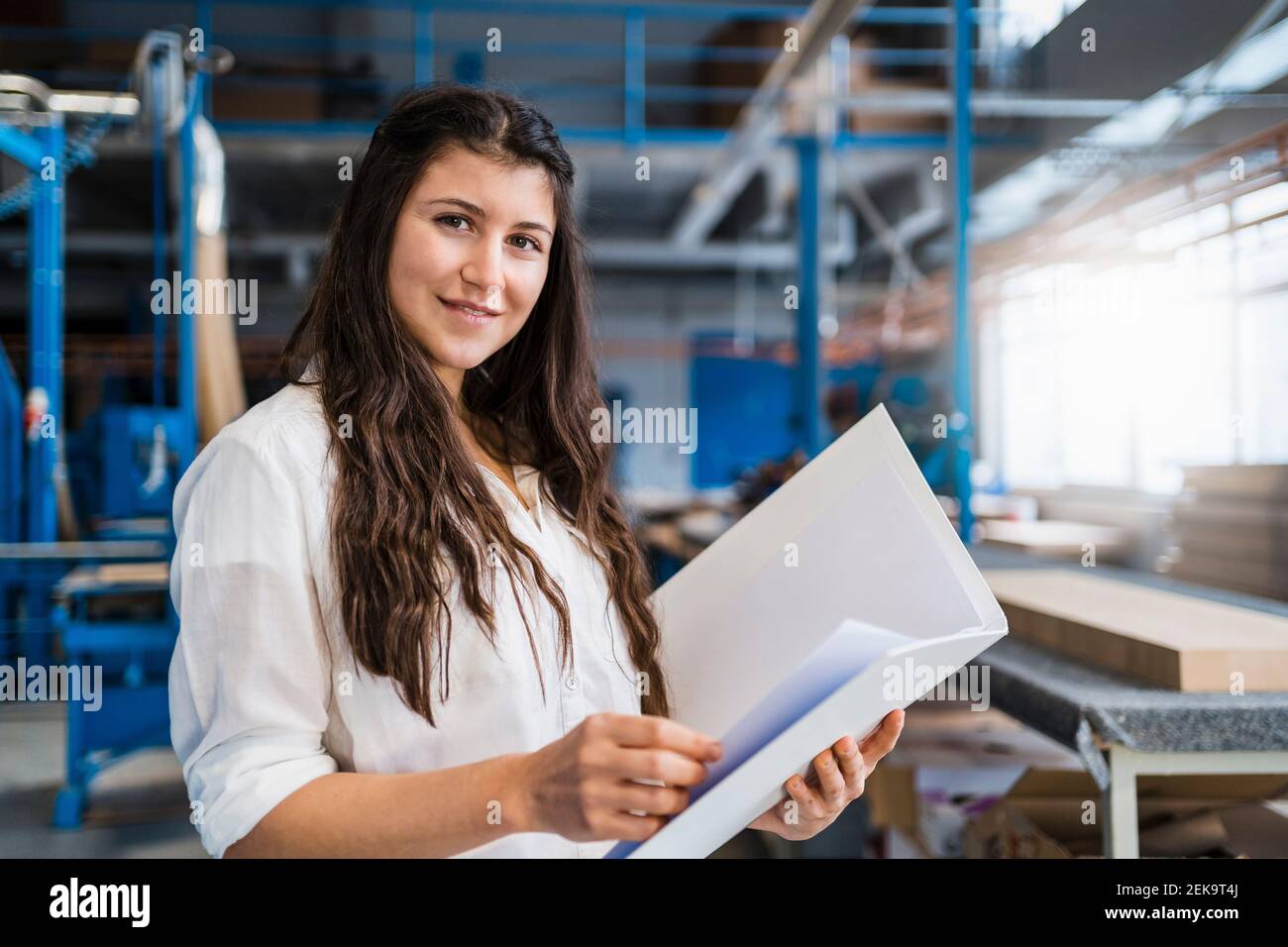 Lächelndes Know-how, das Papierkram überprüft, während man in der Industrie steht Stockfoto