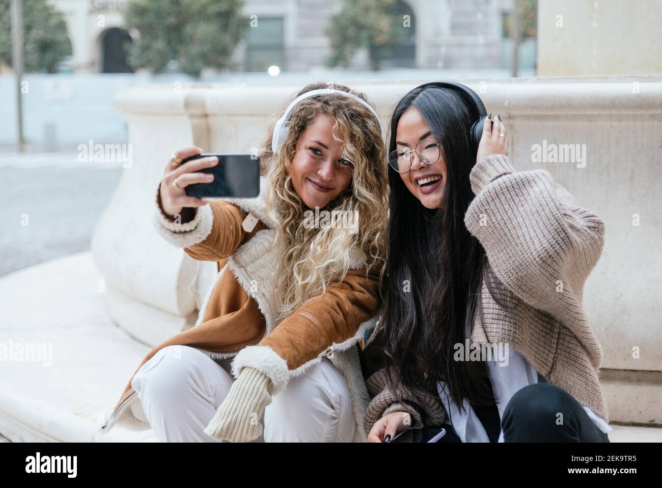 Fröhliche Freundinnen, die Selfie über das Smartphone machen, während sie zuhören Musik über Kopfhörer Stockfoto