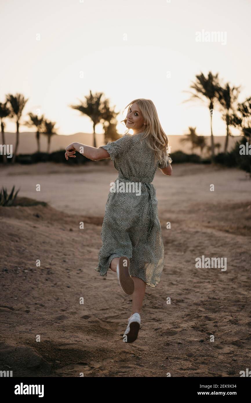 Glückliche Frau in der Luft beim Tanzen über Sand während Sonnenuntergang Stockfoto