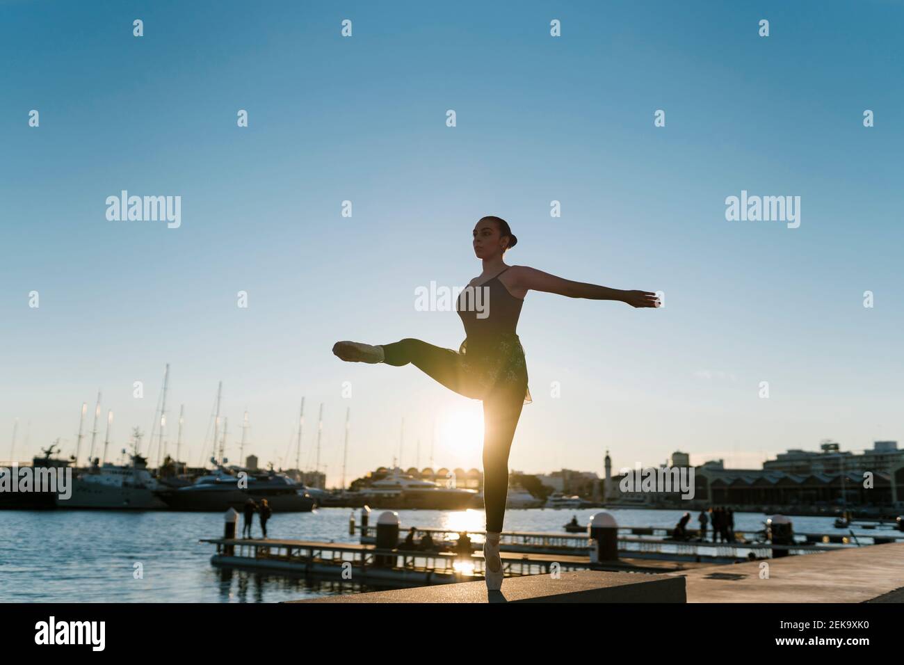 Junge Tänzerin balanciert auf einem Bein während des Übens an marina bei Sonnenuntergang Stockfoto