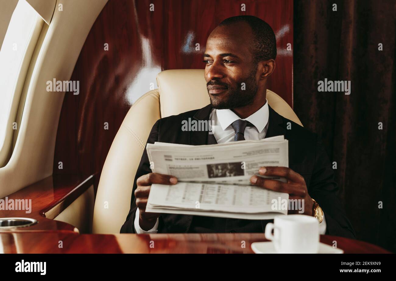 Männlicher Unternehmer, der aus dem Fenster schaut, während er Zeitung hält Privatjet Stockfoto