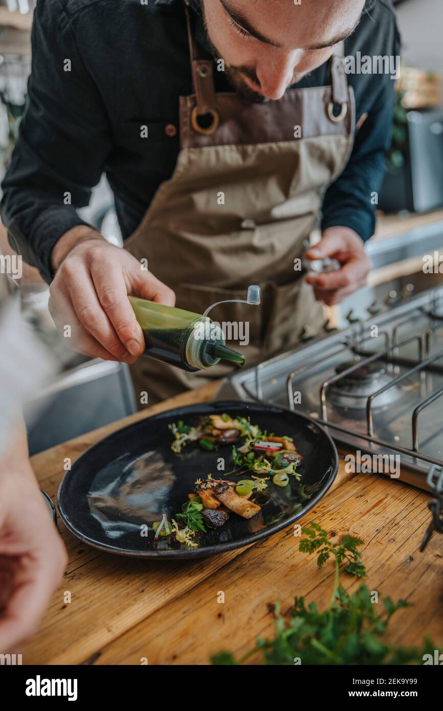 Männliche Expertise garnieren Sauce auf gekochten Lebensmitteln, während im Stehen Küche Stockfoto