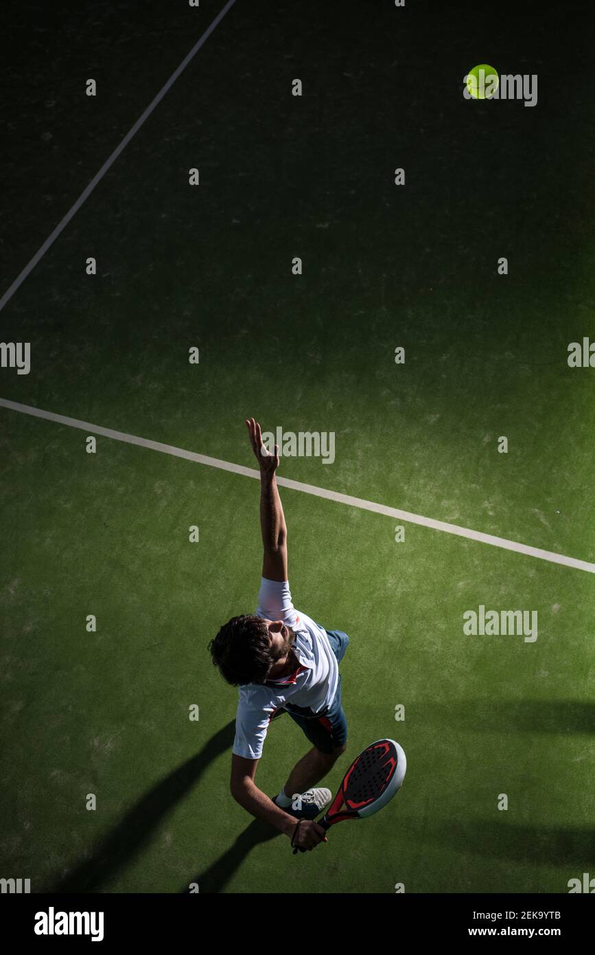 Männlicher Athlet, der den Ball bedient, während er nachts auf dem Sportplatz Padel-Tennis spielt Stockfoto