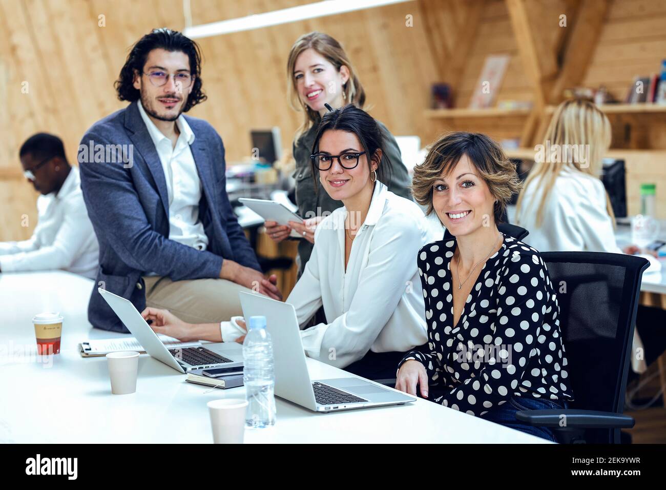 Lächelndes Business-Team mit Laptop, das am Schreibtisch in Coworking Place kreative Ideen entwickelt Stockfoto