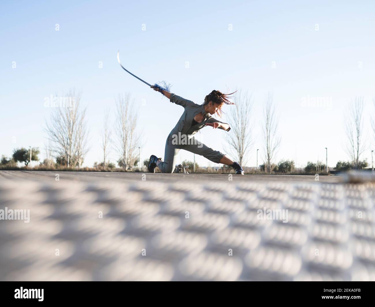 Junge Frau mit Schwert übt Kampfkunst im Park gegen Der Himmel ist klar Stockfoto
