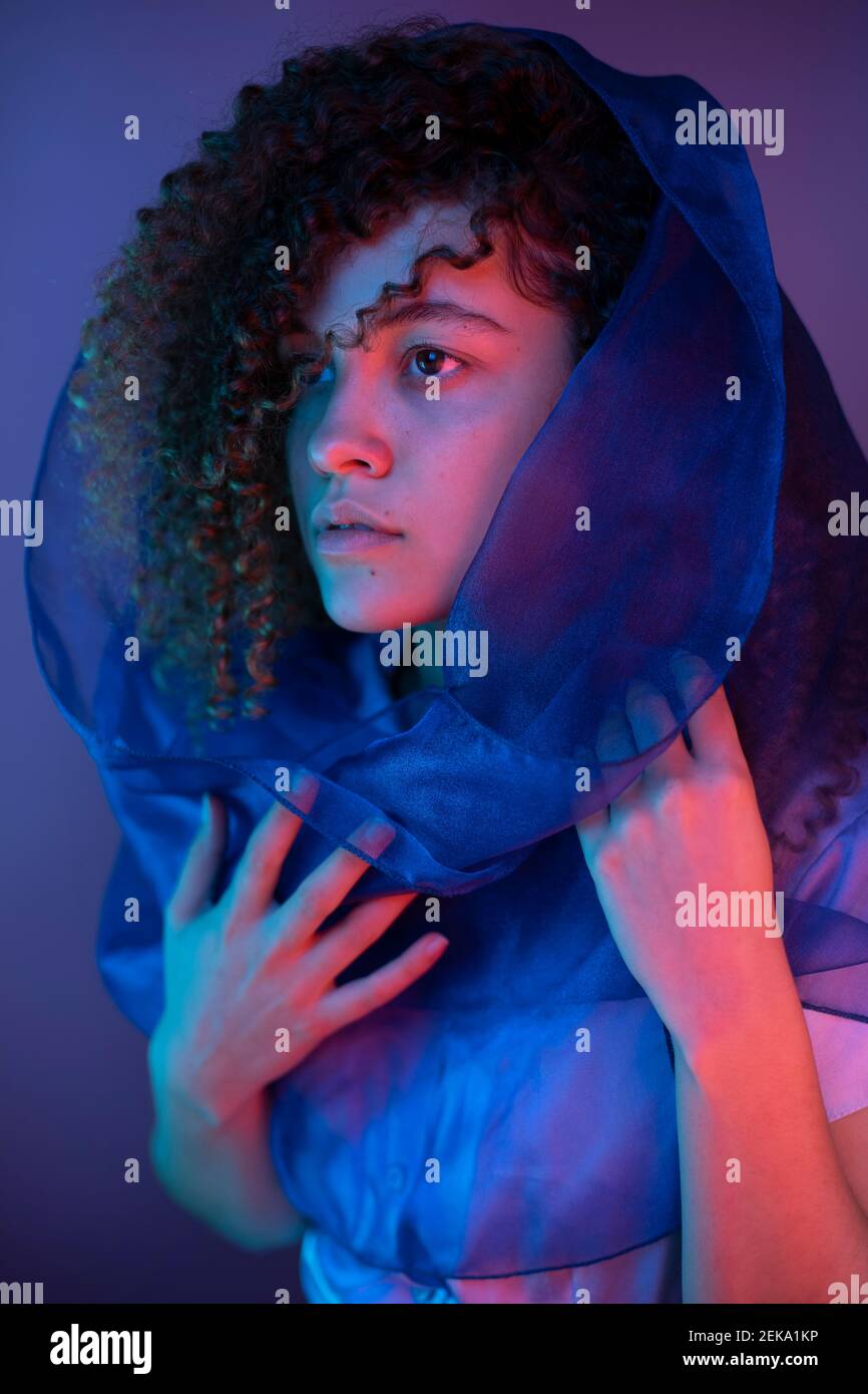 Junge Frau mit Schal weg schauen, während sie bei lila stehen Hintergrund Stockfoto