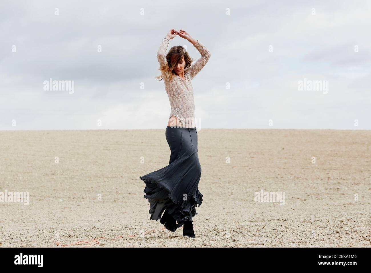 Frau trägt Rock mit erhobenen Armen tanzen am Strand gegen Himmel Stockfoto