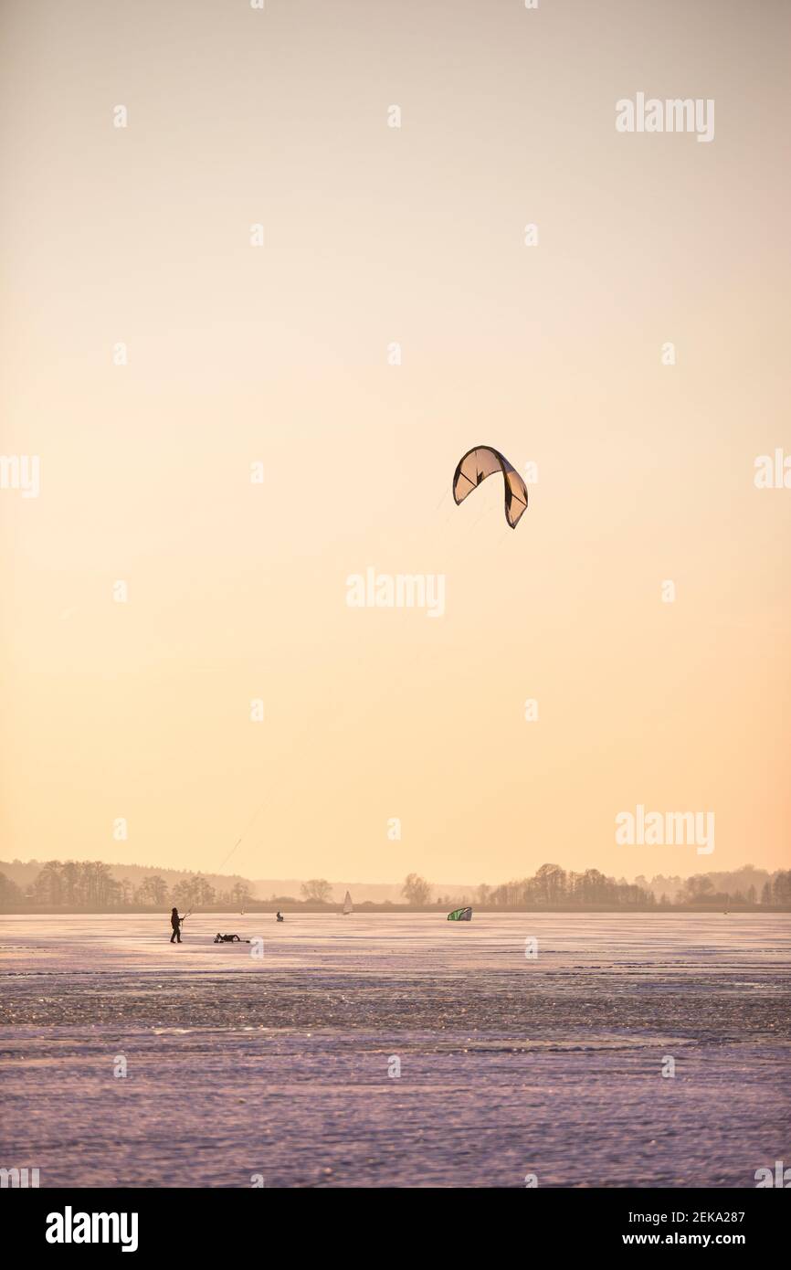 Deutschland, Brandenburg, Rangsdorf, Winterlandschaft mit gefrorenem See, Menschen spielen mit Drachen Stockfoto