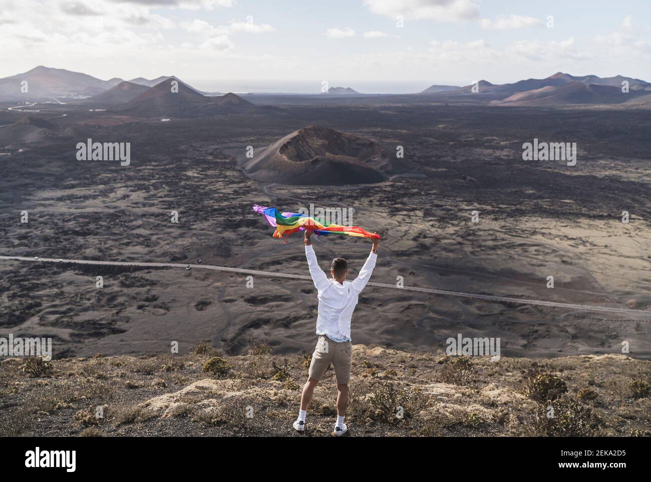 Junger männlicher Tourist, der während der Ferien am Vulkan El Cuervo auf Lanzarote, Spanien, Regenbogenflaise schwenkt Stockfoto