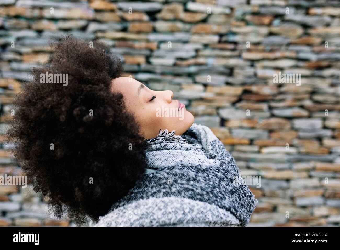 Junge Frau mit geschlossenen Augen in warmer Kleidung von Stein Wand Stockfoto