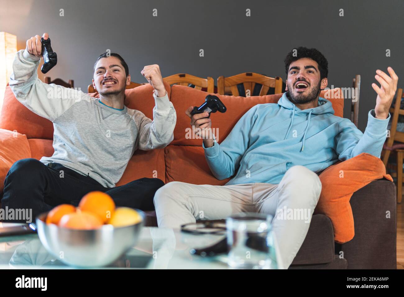 Junge konkurrierende Freunde spielen Videospiel sitzen auf dem Sofa in Wohnzimmer Stockfoto