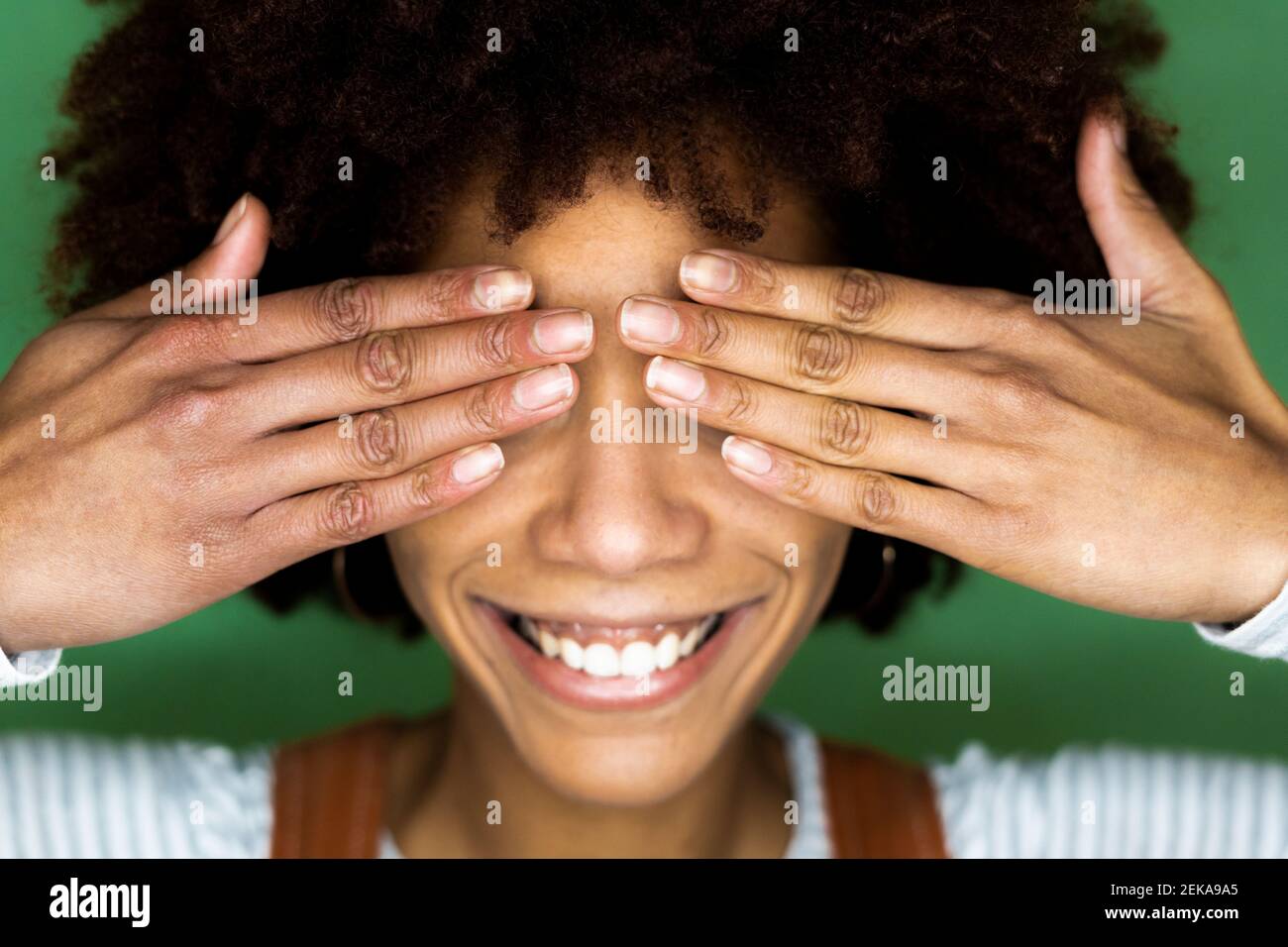 Glückliche junge Frau, die die Augen mit der Hand gegen die grüne Wand bedeckt In neuem Zuhause Stockfoto