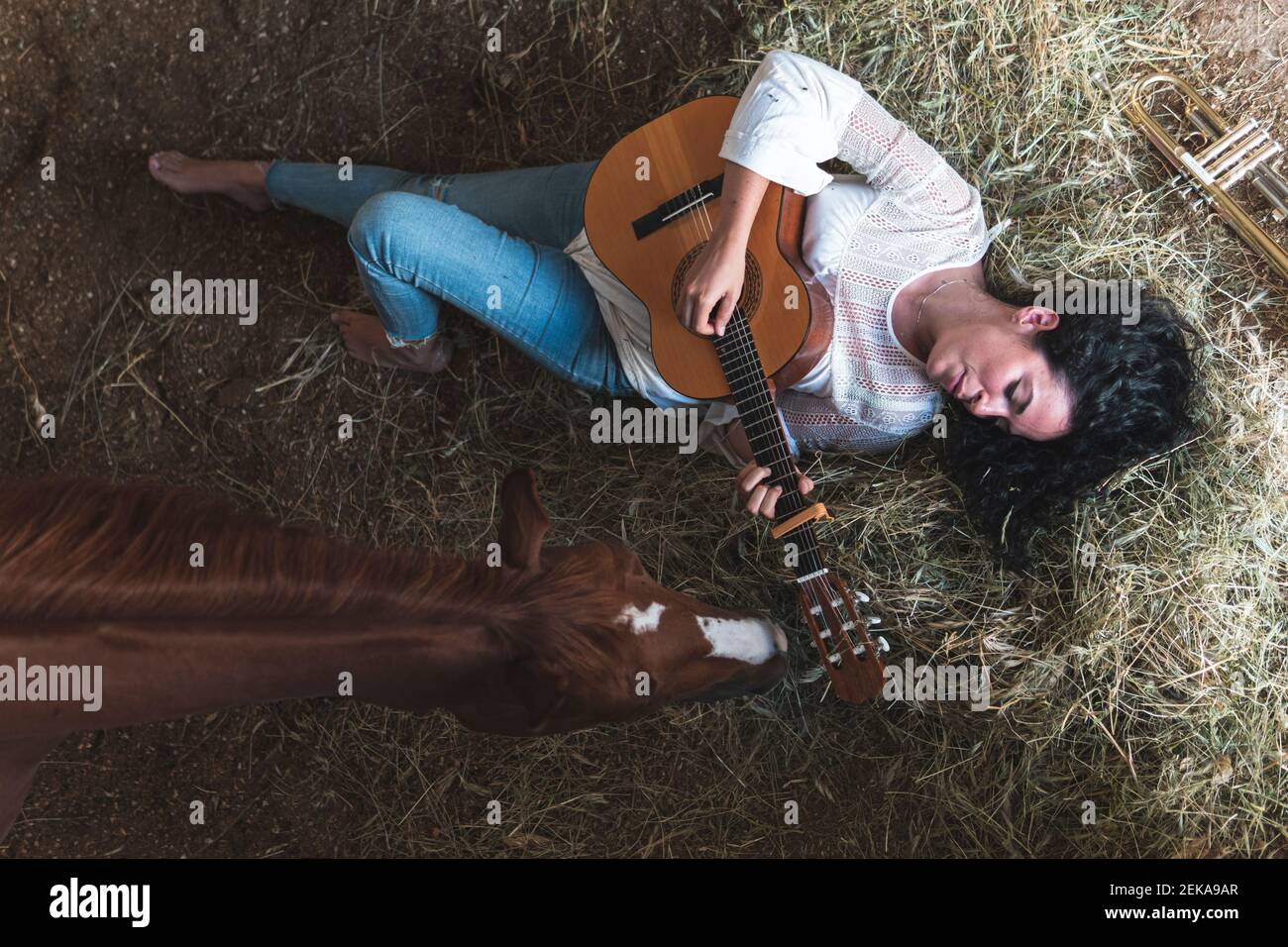 Frau mittleren Erwachsenen mit Pferd Gitarre spielen, während liegend Heu im Stall Stockfoto