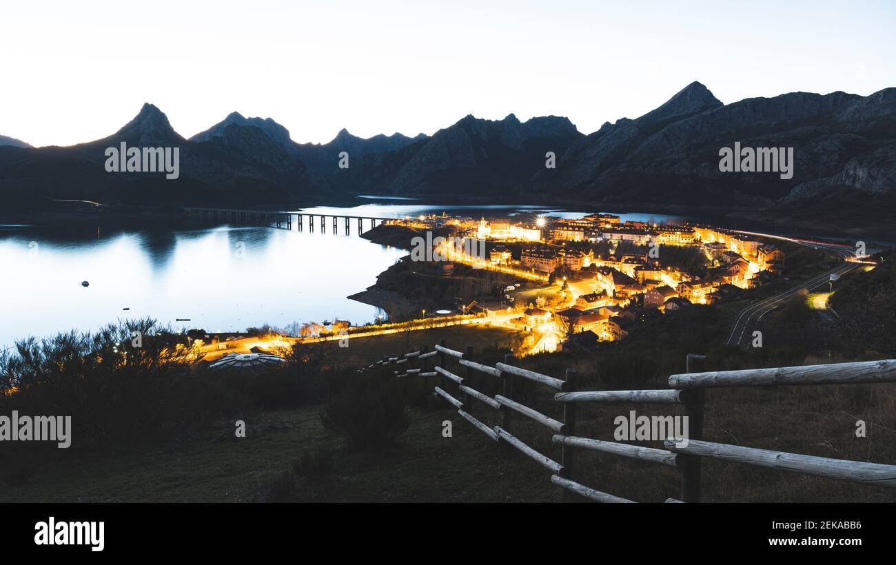 Beleuchtetes Dorf am See gegen Berge in der Dämmerung Stockfoto