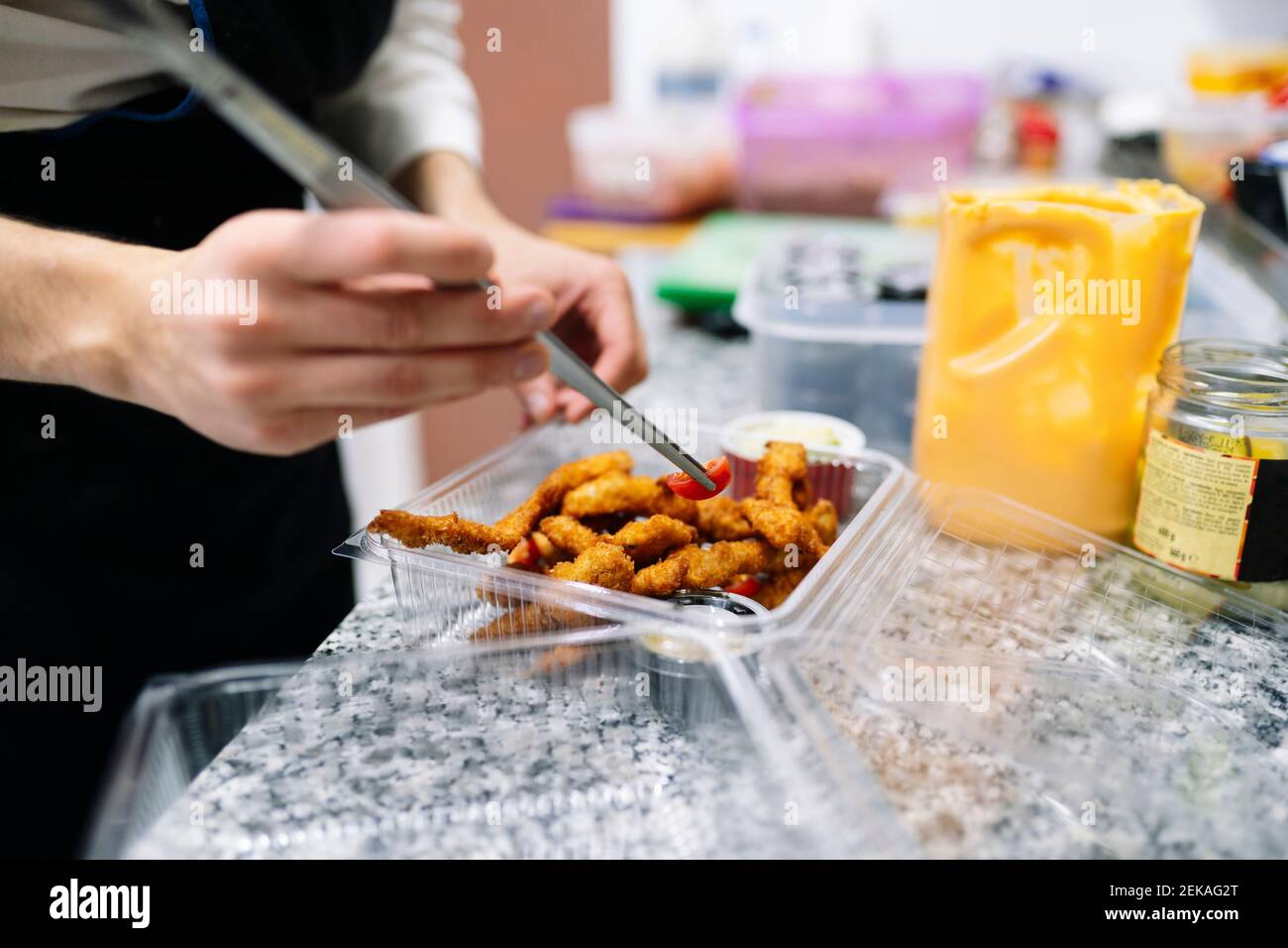 Junger männlicher Koch bereitet Essen in Plastikbehälter auf der Theke Im Restaurant Stockfoto