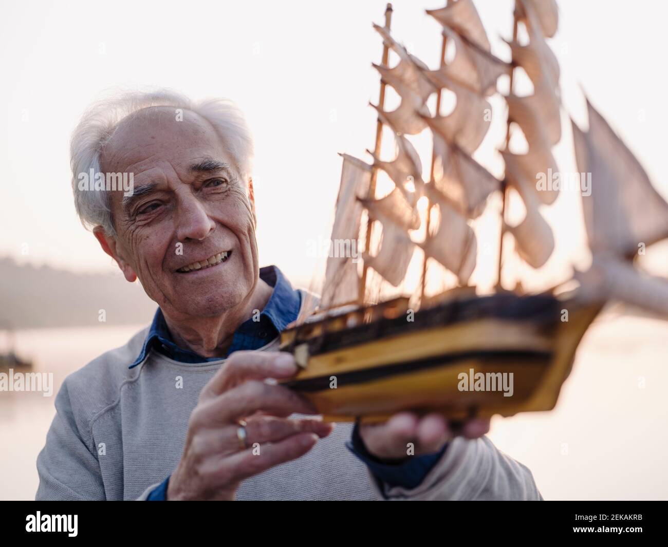 Lächelnder Mann, der Segelschiff Spielzeug untersucht, während er im Freien steht Stockfoto