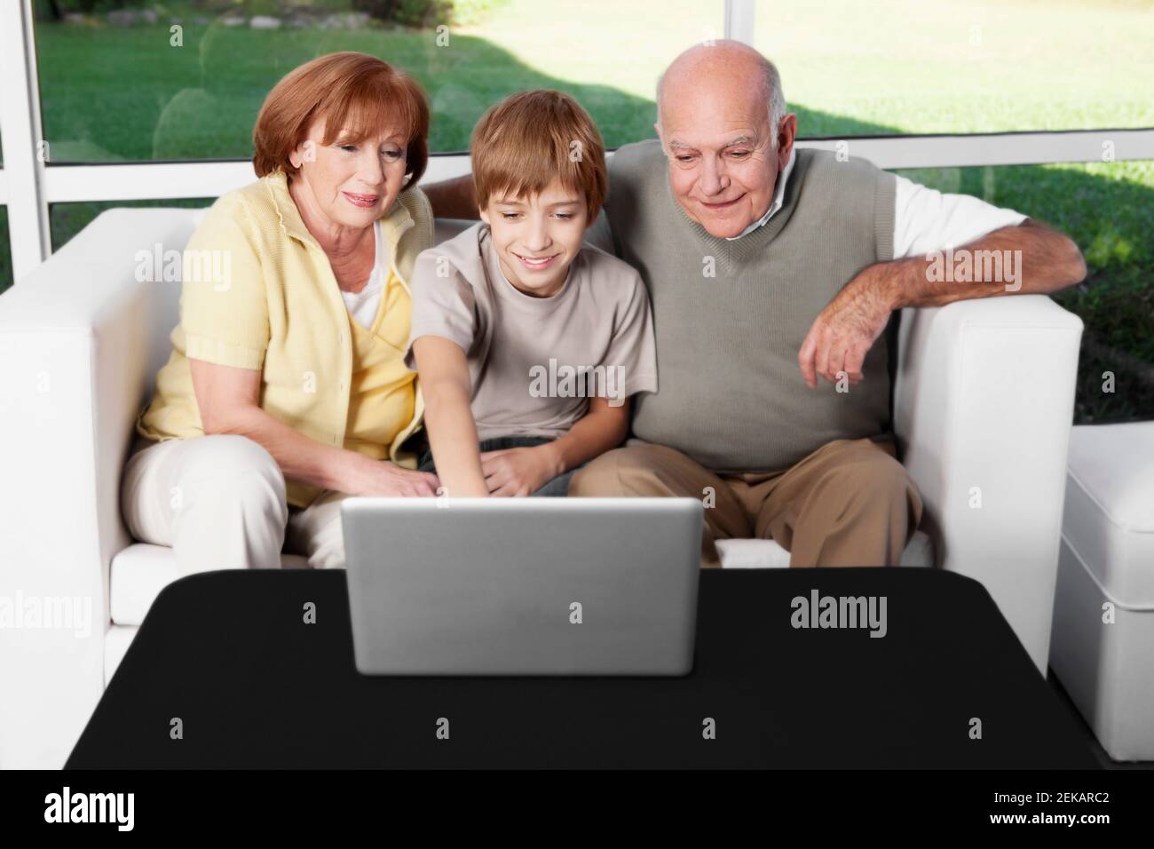 Junge sitzt mit seinen Großeltern mit einem Laptop Stockfoto