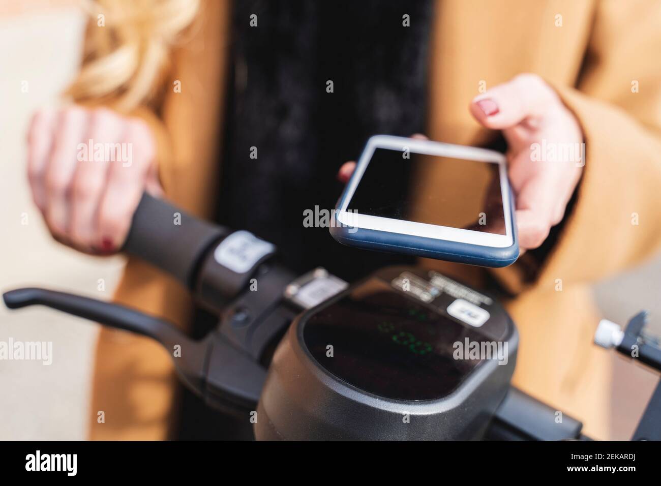 Frau mit Smartphone für die Entriegelung elektrischer Roller schieben Stockfoto