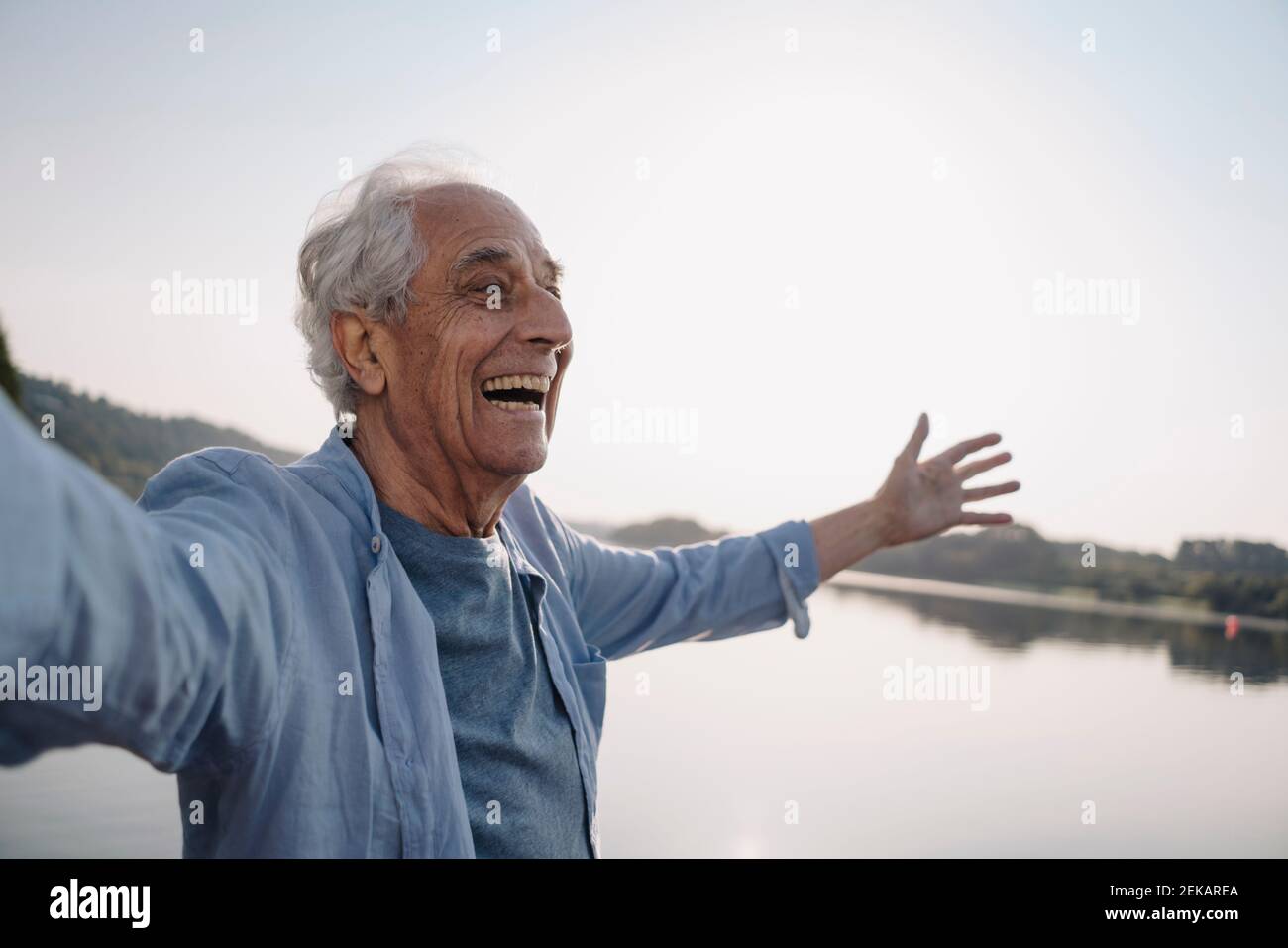 Sorgenfreier älterer Mann, der mit ausgestreckten Armen gegen den Himmel steht Stockfoto