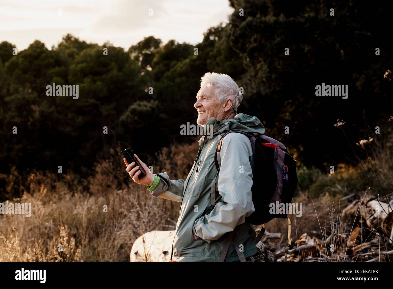 Lächelnder älterer Mann mit Mobiltelefon, das im Stehen wegschaut Am Wochenende eingereicht Stockfoto