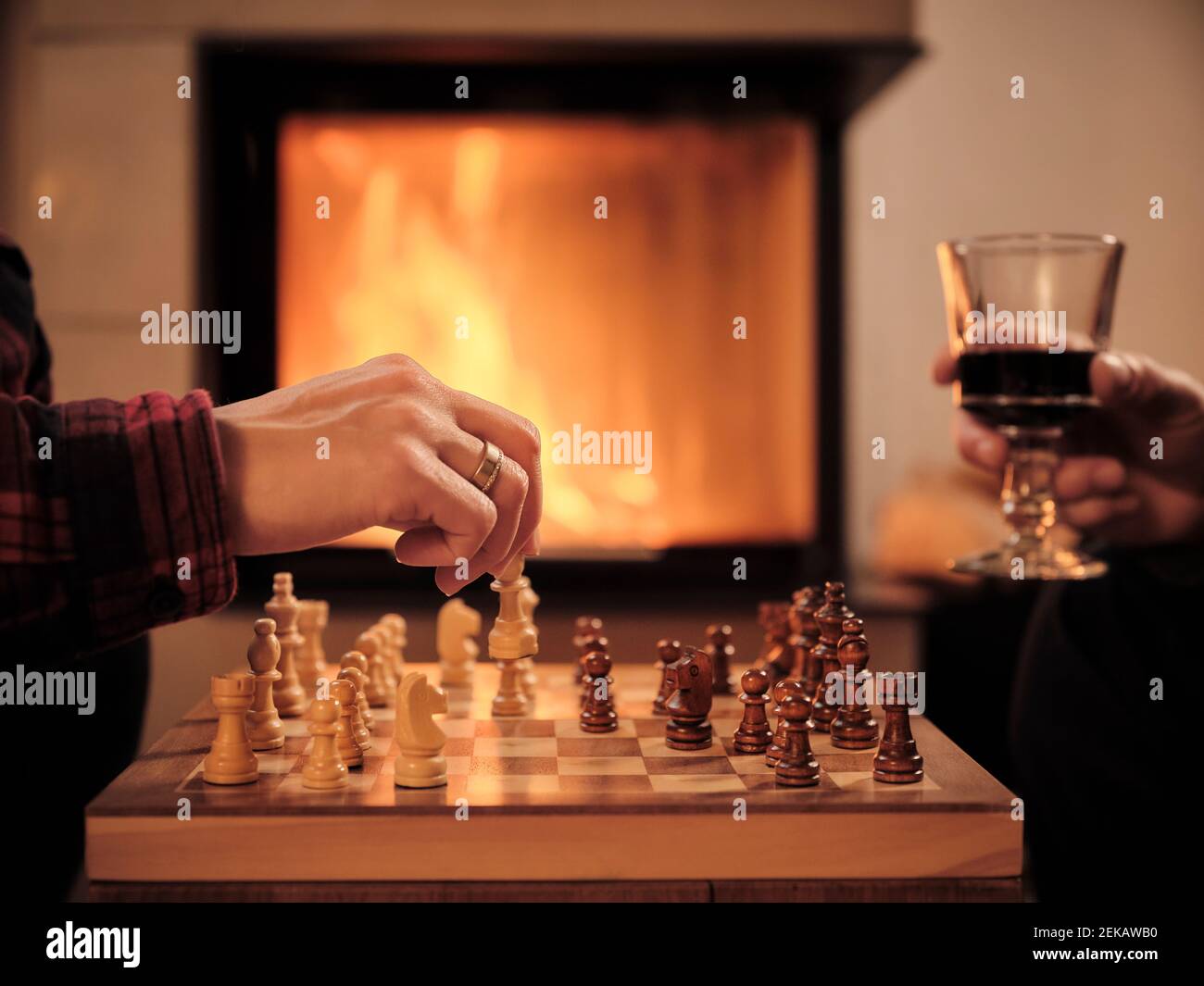 Reifer Mann mit Weinglas, während Frau Schach spielen Kamin im Wohnzimmer Stockfoto