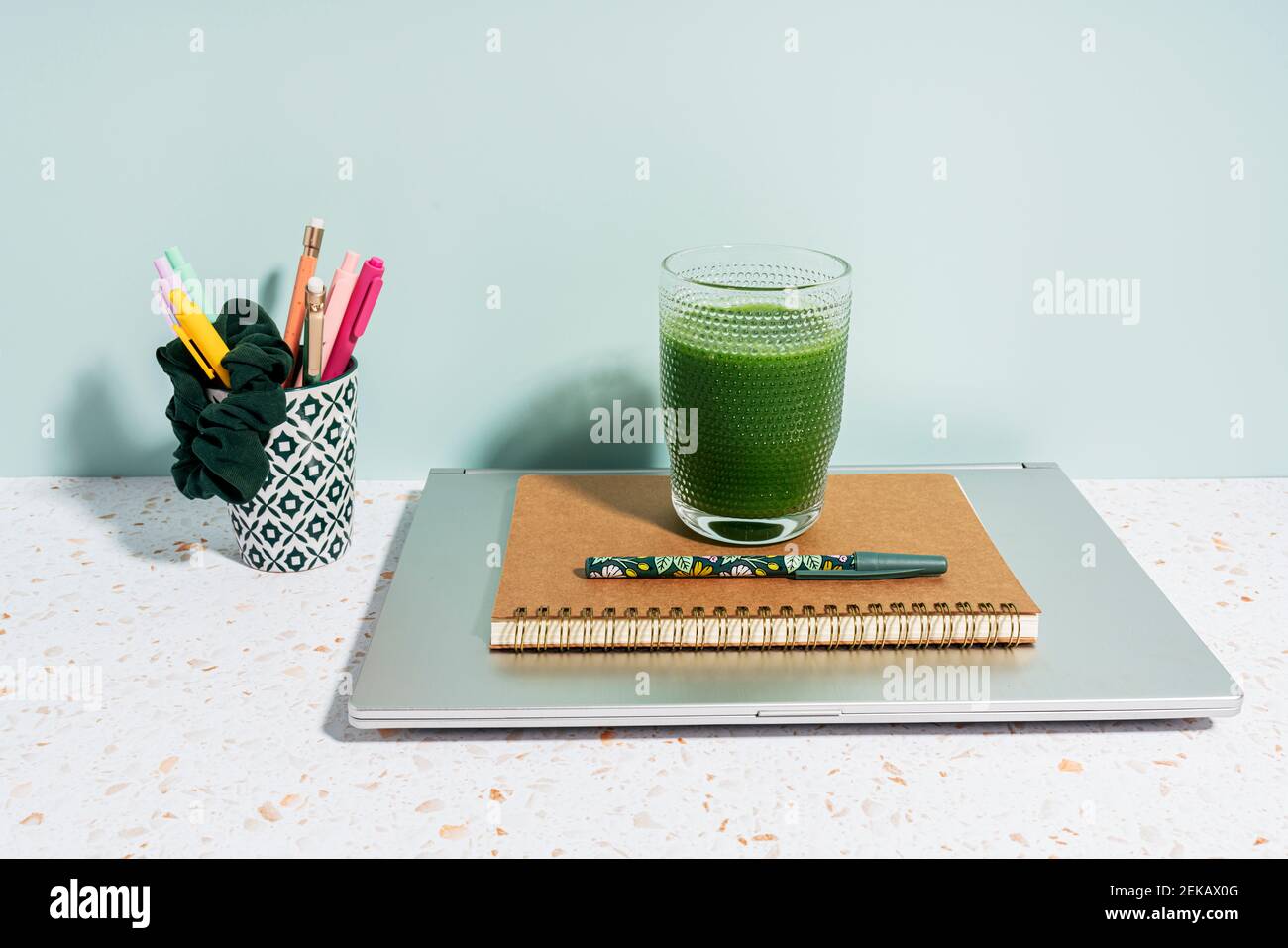 Gesunder grüner Saft, Buch, Stift und Laptop über Schreibtisch gegen Wand zu Hause Stockfoto