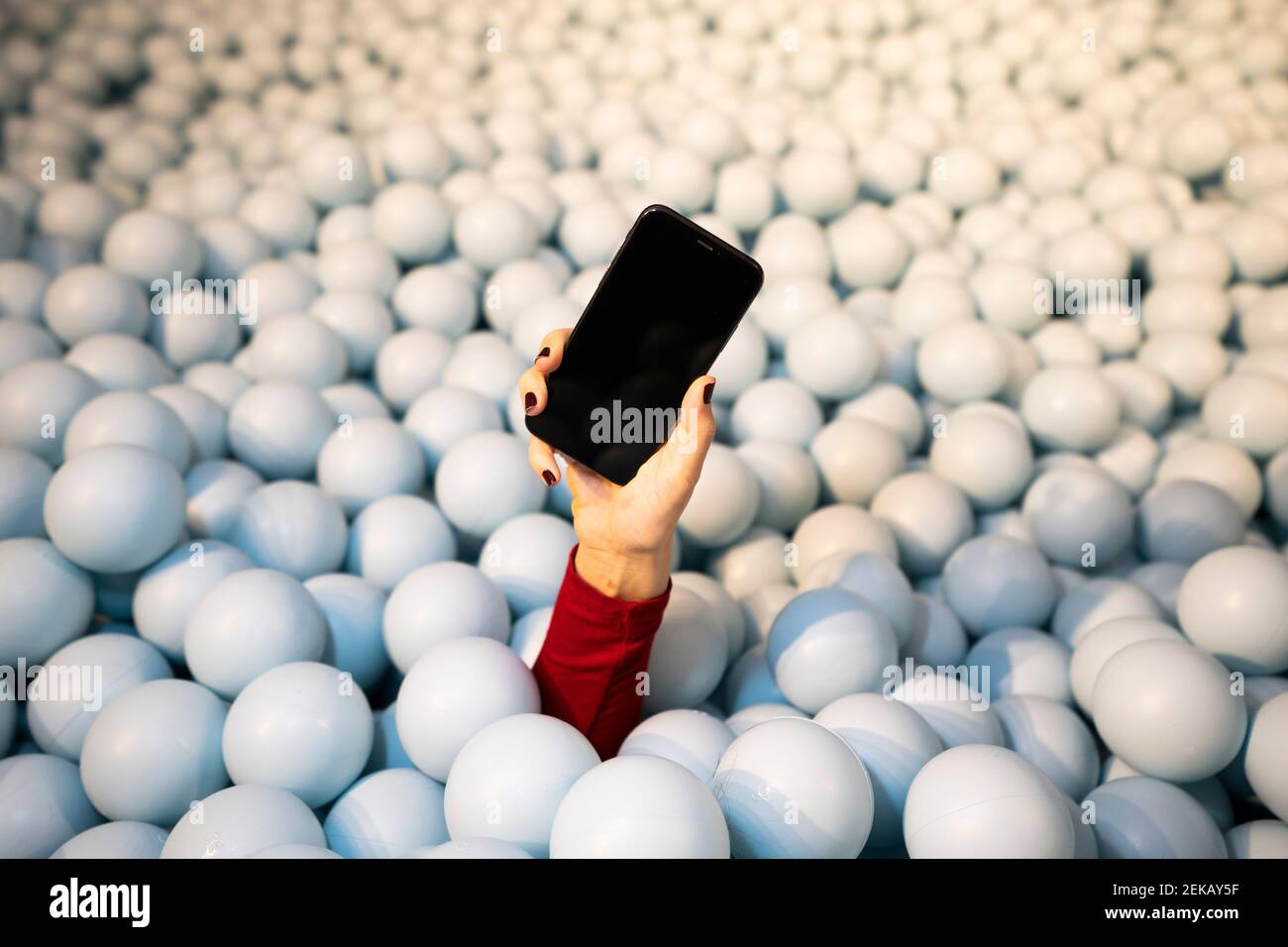 Hand einer jungen Frau, die das Handy in der Kugelgrube hält Stockfoto