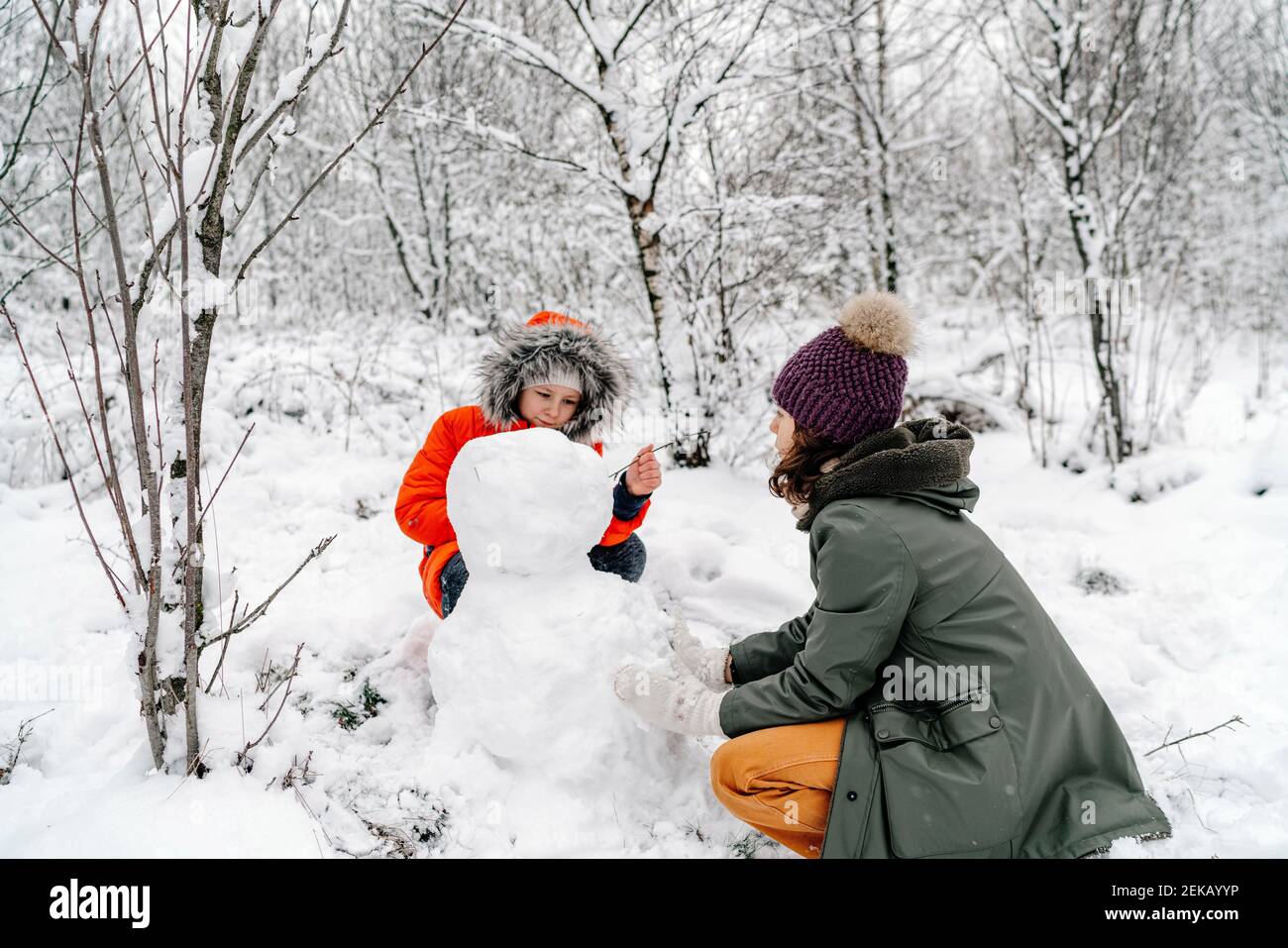 Mädchen mit Teenager-Schwester machen Schneemann im Wald Stockfoto