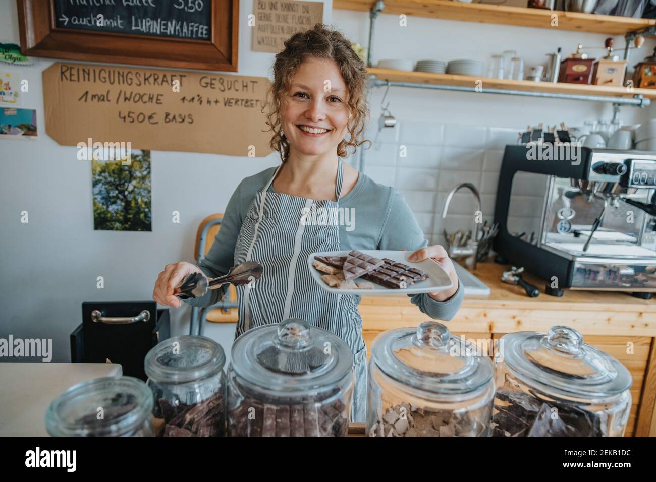 Glückliche junge Frau Angestellte hält Teller voller Schokolade, während Im Café stehen Stockfoto