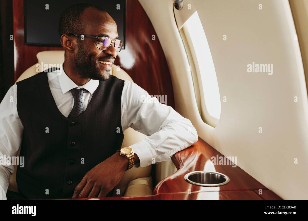 Lächelnder Geschäftsmann, der durch das Fenster schaut, während er im Privatjet reist Stockfoto