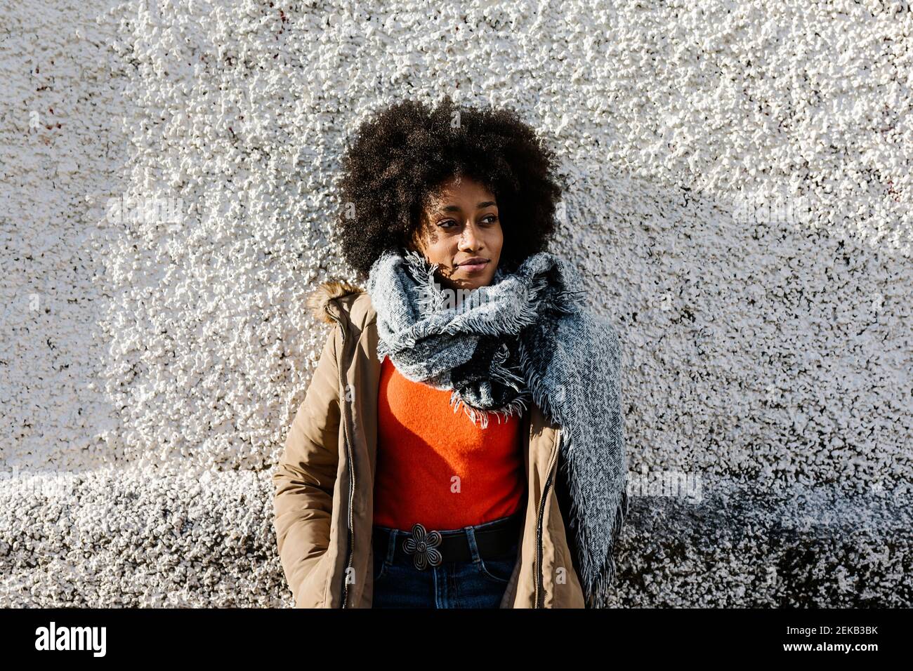 Afro junge Frau mit Händen in Taschen gegen strukturierte Wand Stockfoto