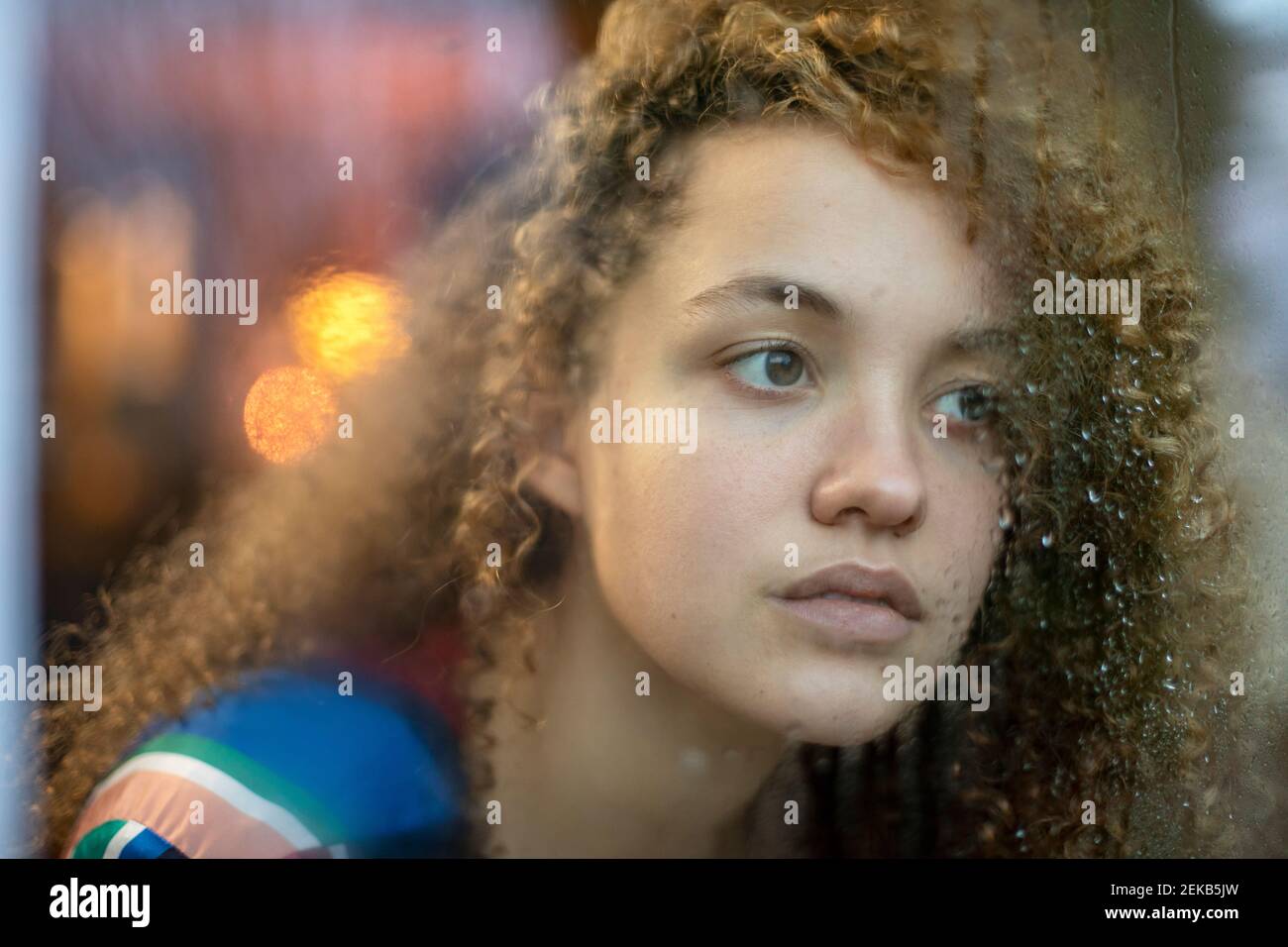 Betrachten einer jungen Frau, die durch ein nasses Fenster zu Hause schaut Stockfoto