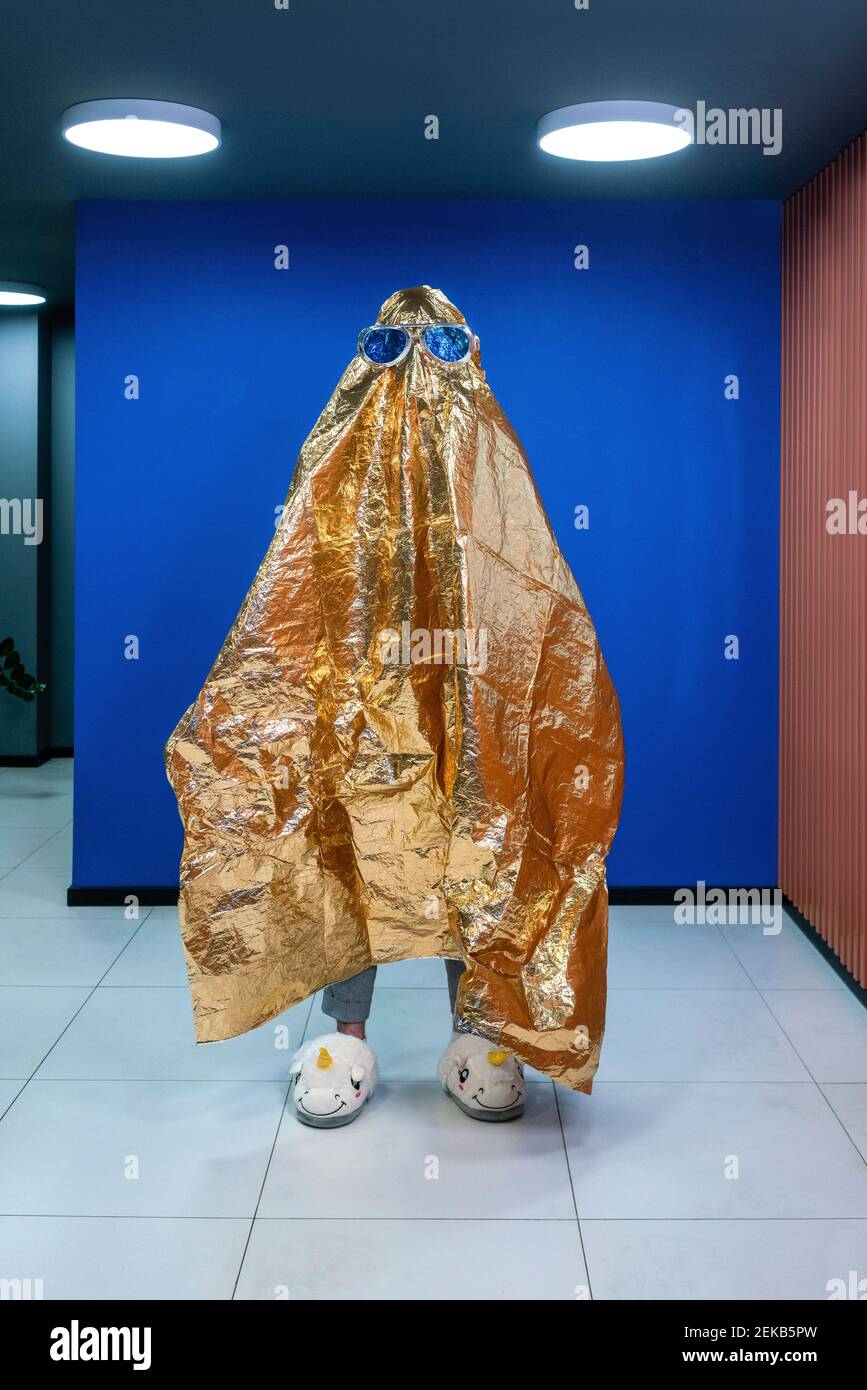 Kreative Geschäftsmann in Neuheit Gläser in Gold Farbe Verpackung bedeckt Papier gegen blaue Wand im Büro Stockfoto