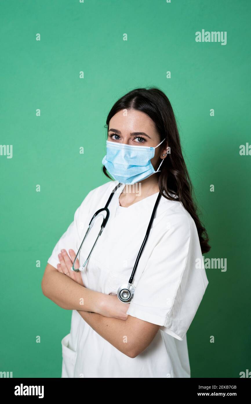 Junge Ärztin mit Armen, die von grünem Hintergrund gekreuzt sind studio Stockfoto