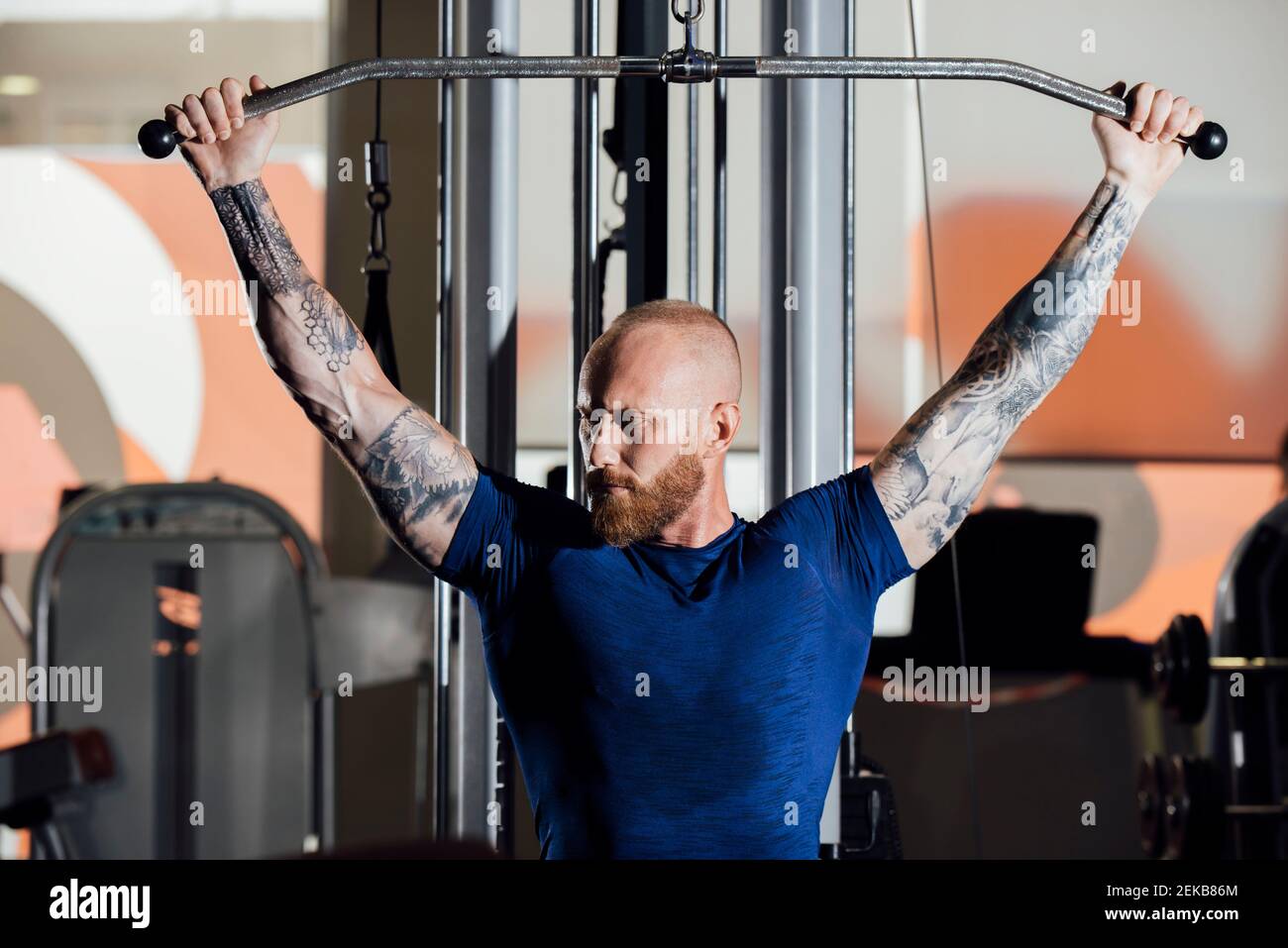 Sportler trainieren, während sie auf der Lat Pull-down-Maschine sitzen Fitnessraum Stockfoto