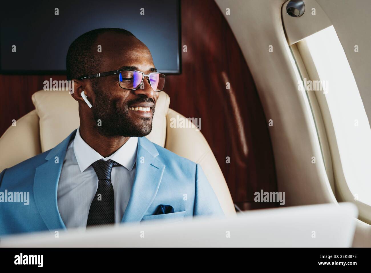 Lächelnder männlicher Unternehmer mit geschlossenen Augen im Flugzeug Stockfoto
