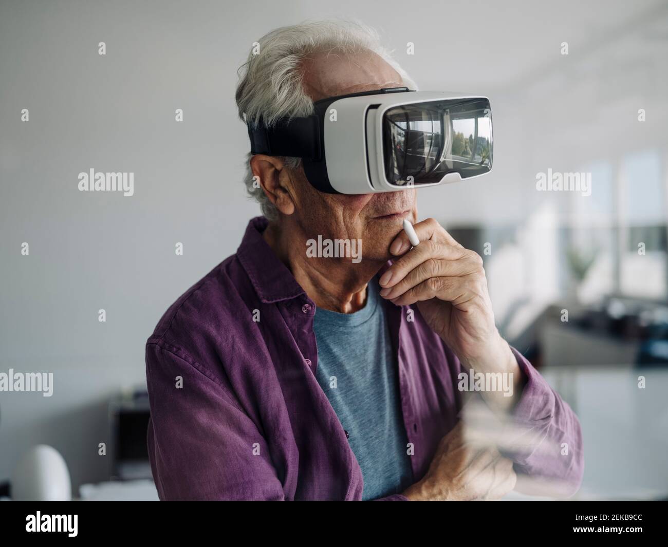 Durchdachter Geschäftsmann mit Hand auf Chi mit Virtual-Reality-Headset Im Büro stehen Stockfoto