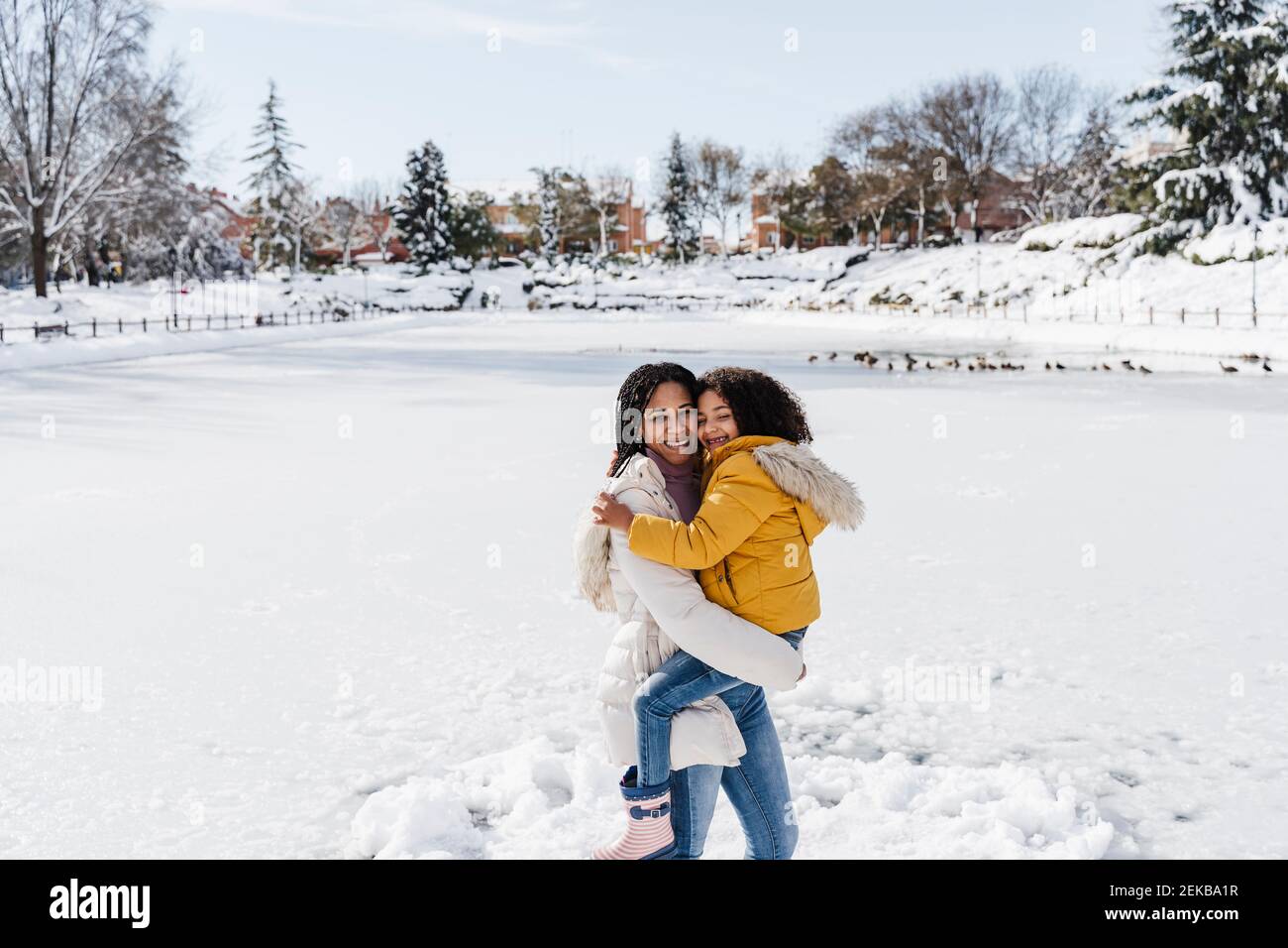 Lächelnde Mutter, die Tochter trägt, während sie im Winter an Land steht Stockfoto